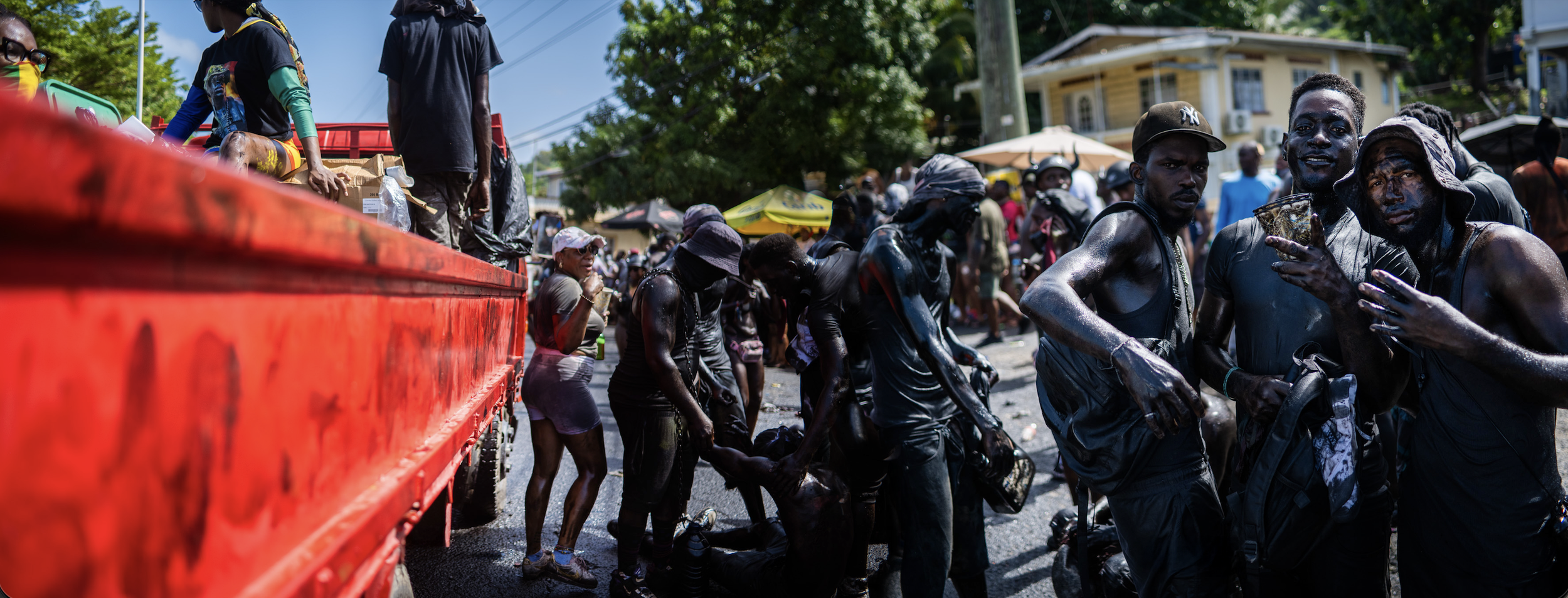 People participating in a water fight or muddy splash event on a city street, with some standing near a red truck and others covered in mud, wearing casual clothing and hats.