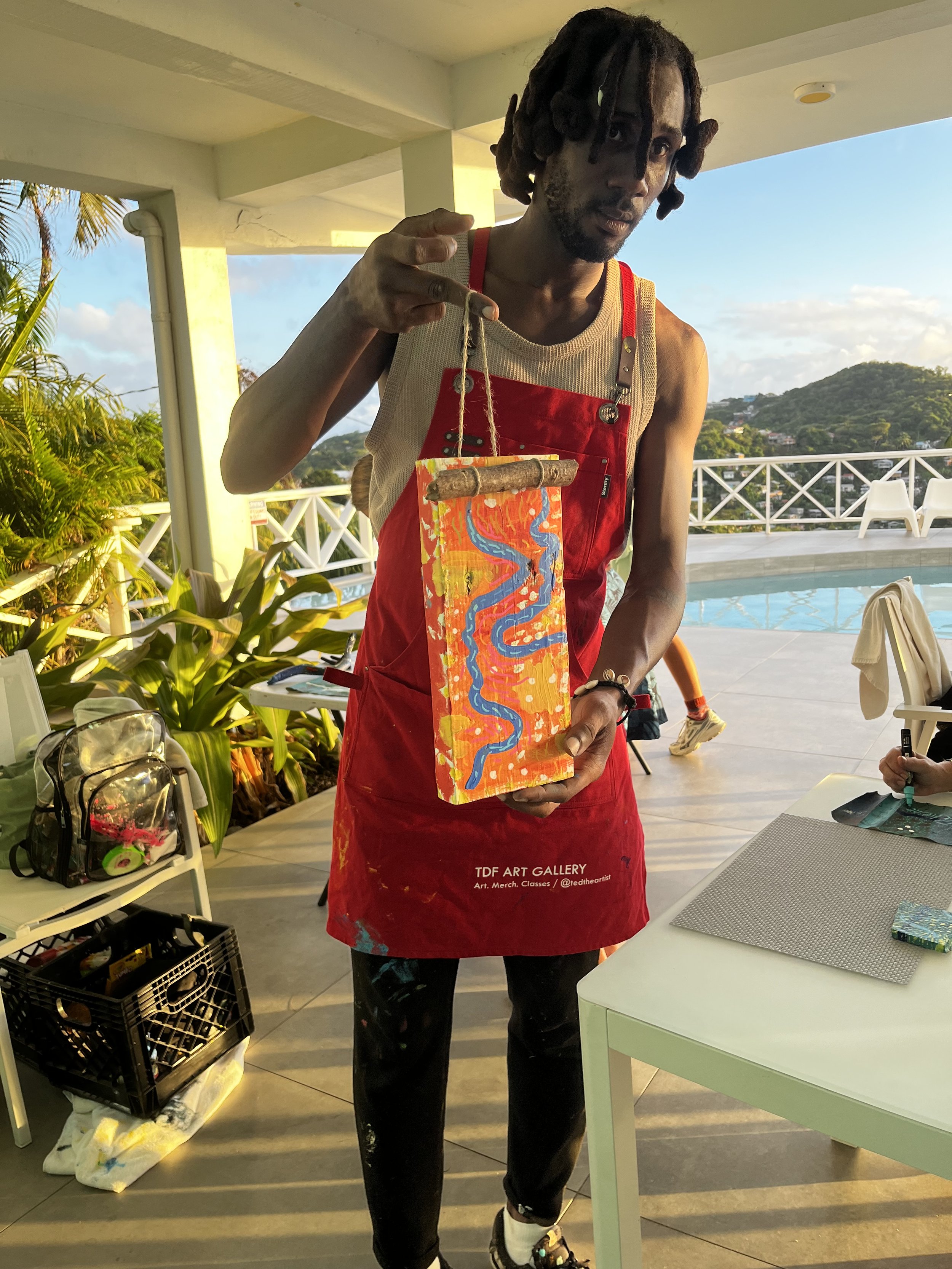 A man wearing a red apron with the text 'TDF Art Gallery' holding a colorful, abstract painted art piece.