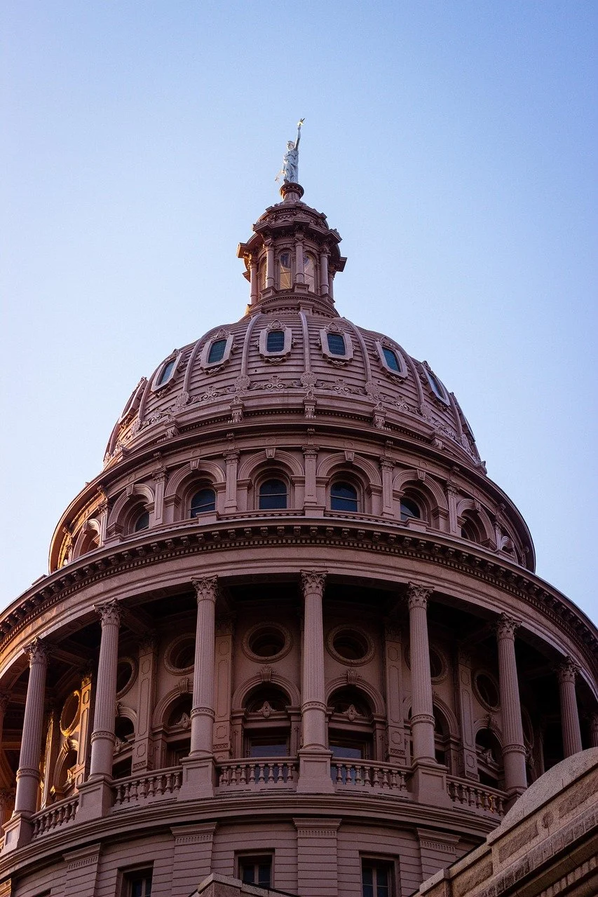 Looking up at the United States Capitol building's dome with sculpture at the top, against a clear blue sky.