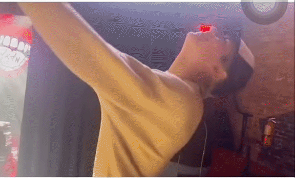 A young man wearing a yellow shirt and a red cap is looking at his phone in an indoor setting.