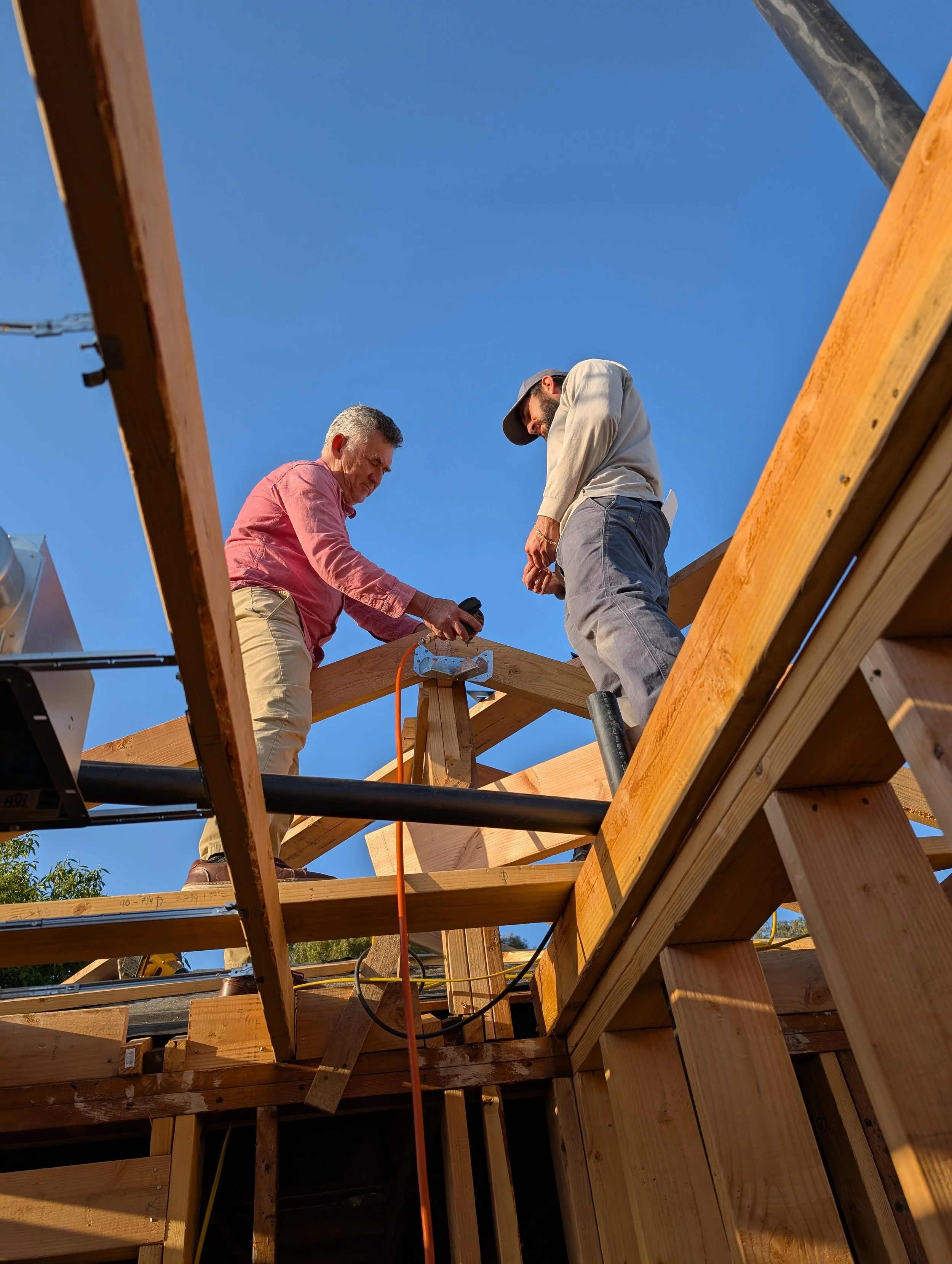 Two men working on a wooden construction frame under a clear blue sky.