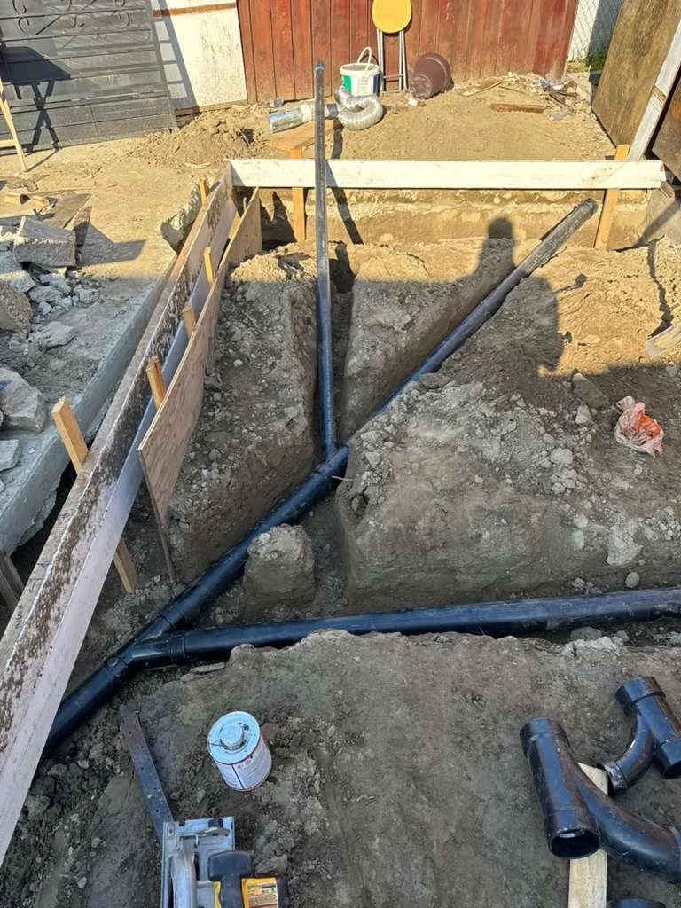 Underground plumbing pipes being installed in a construction site with surrounding dirt and wooden frame.