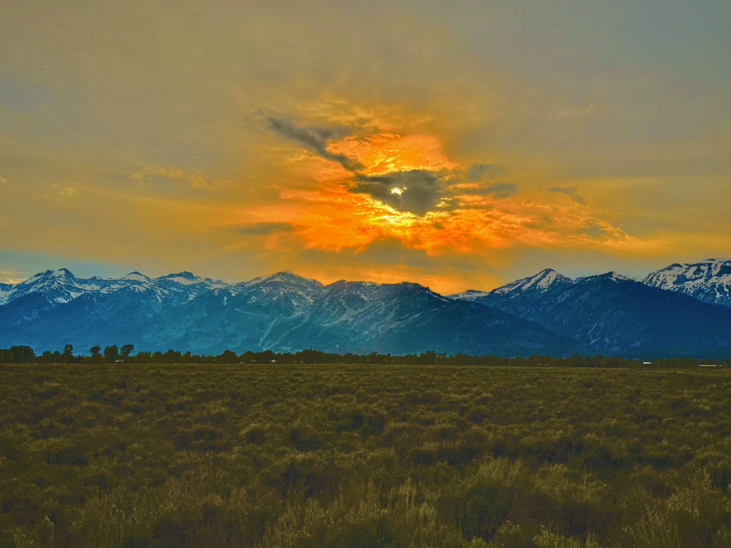 Sunset over snow-capped mountains with a field in the foreground.