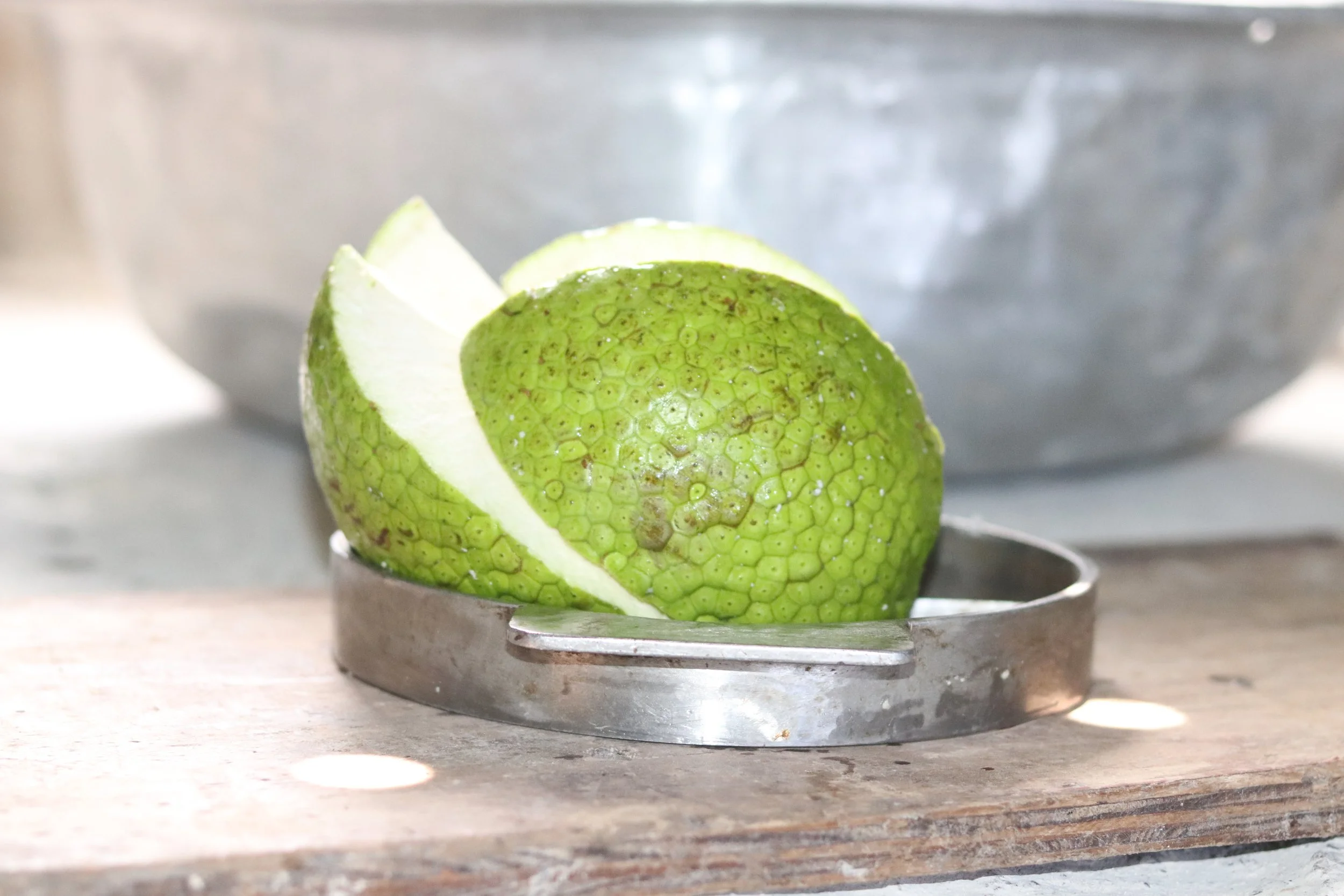 Close-up of a lime partially cut with a metal lime squeezer on a wooden surface.