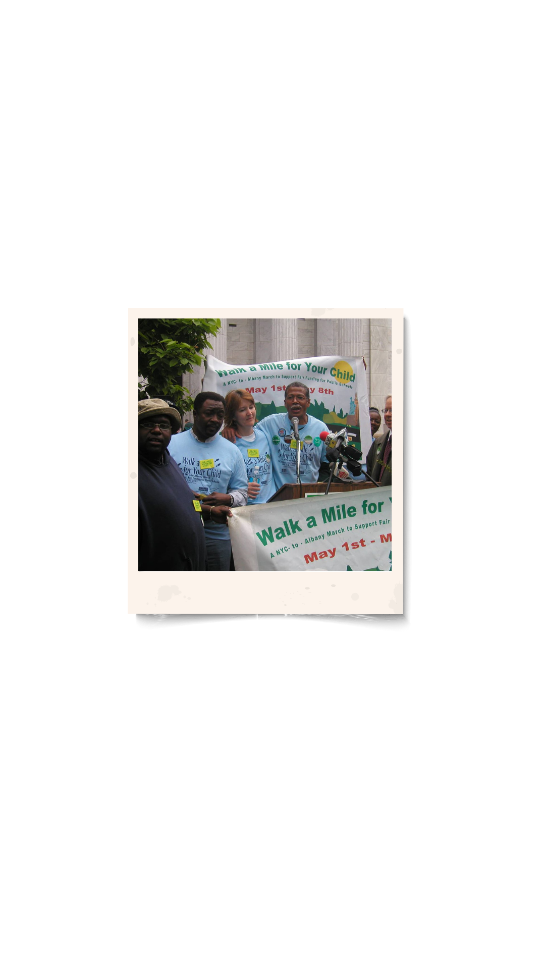 People at a rally supporting a walk for children's education, with a speaker at a podium and banners.