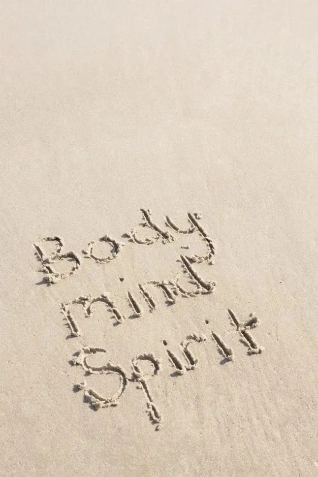 Sand on a beach with the words 'body mind spirit' written in it.