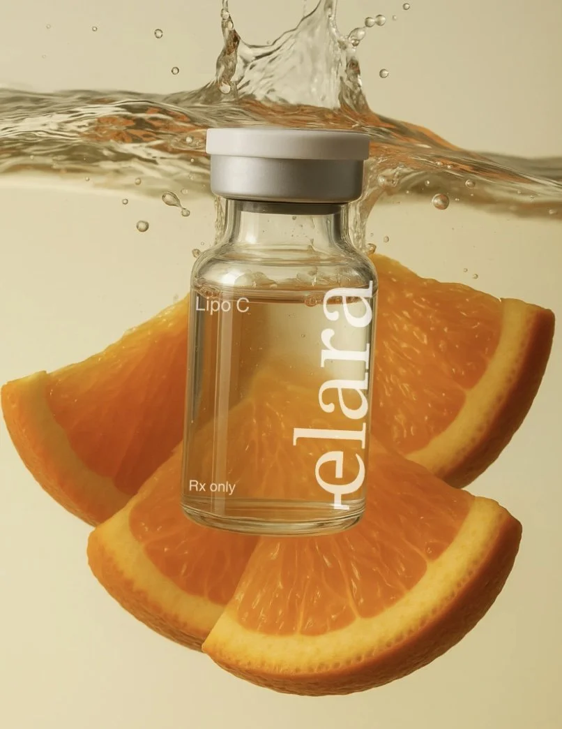 A small vial labeled 'Elara' is floating underwater among sliced orange wedges. The vial is partially submerged, with water splashing at the top.