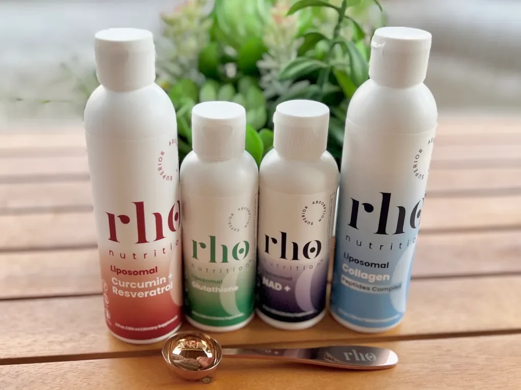 Four bottles of nutritional supplements on a wooden surface with a small spoon in front, in front of a green leafy background.