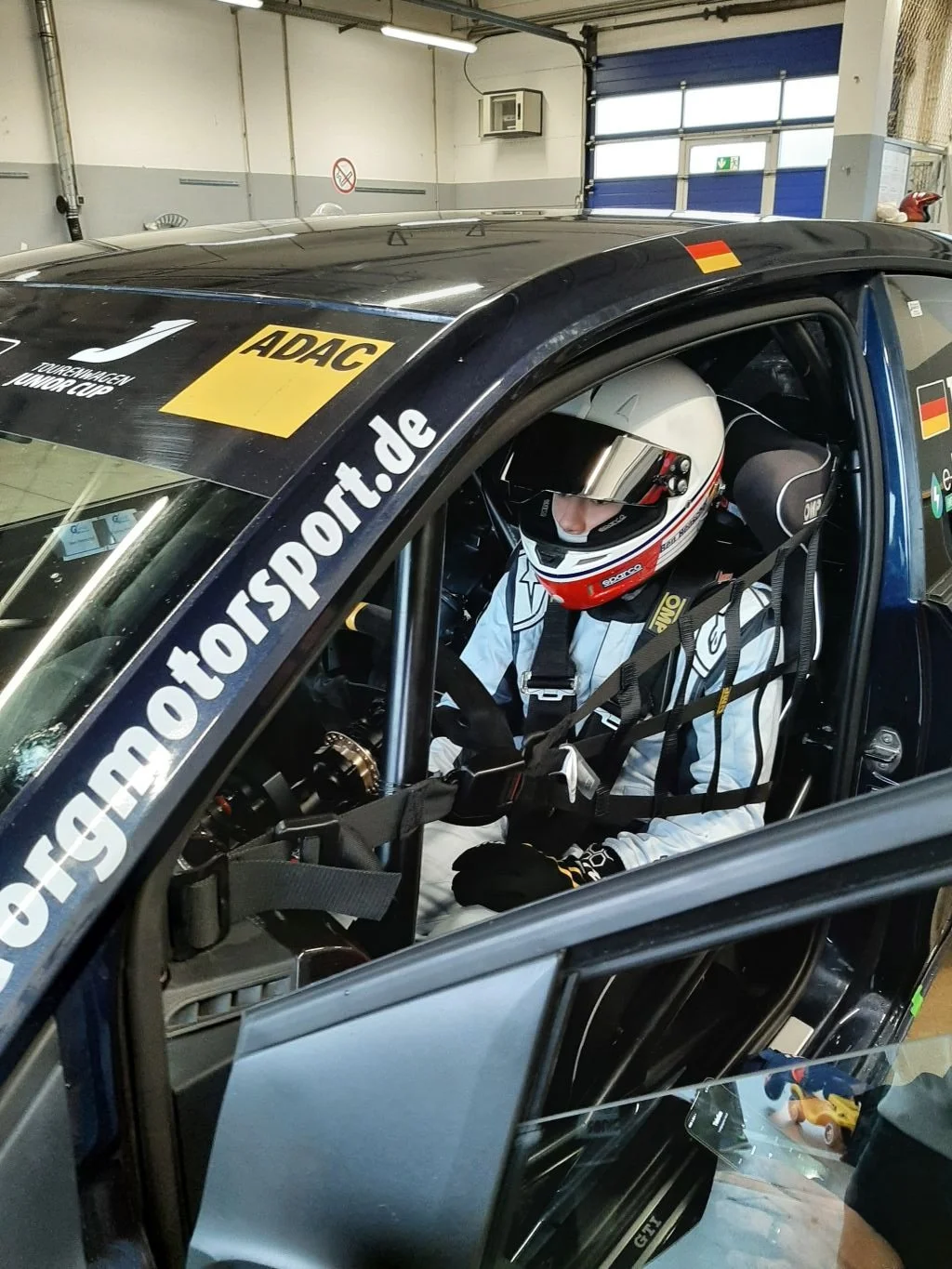 Ein Rennfahrer im Auto, bereit für ein Rennen, mit Helm, in einer Garage.