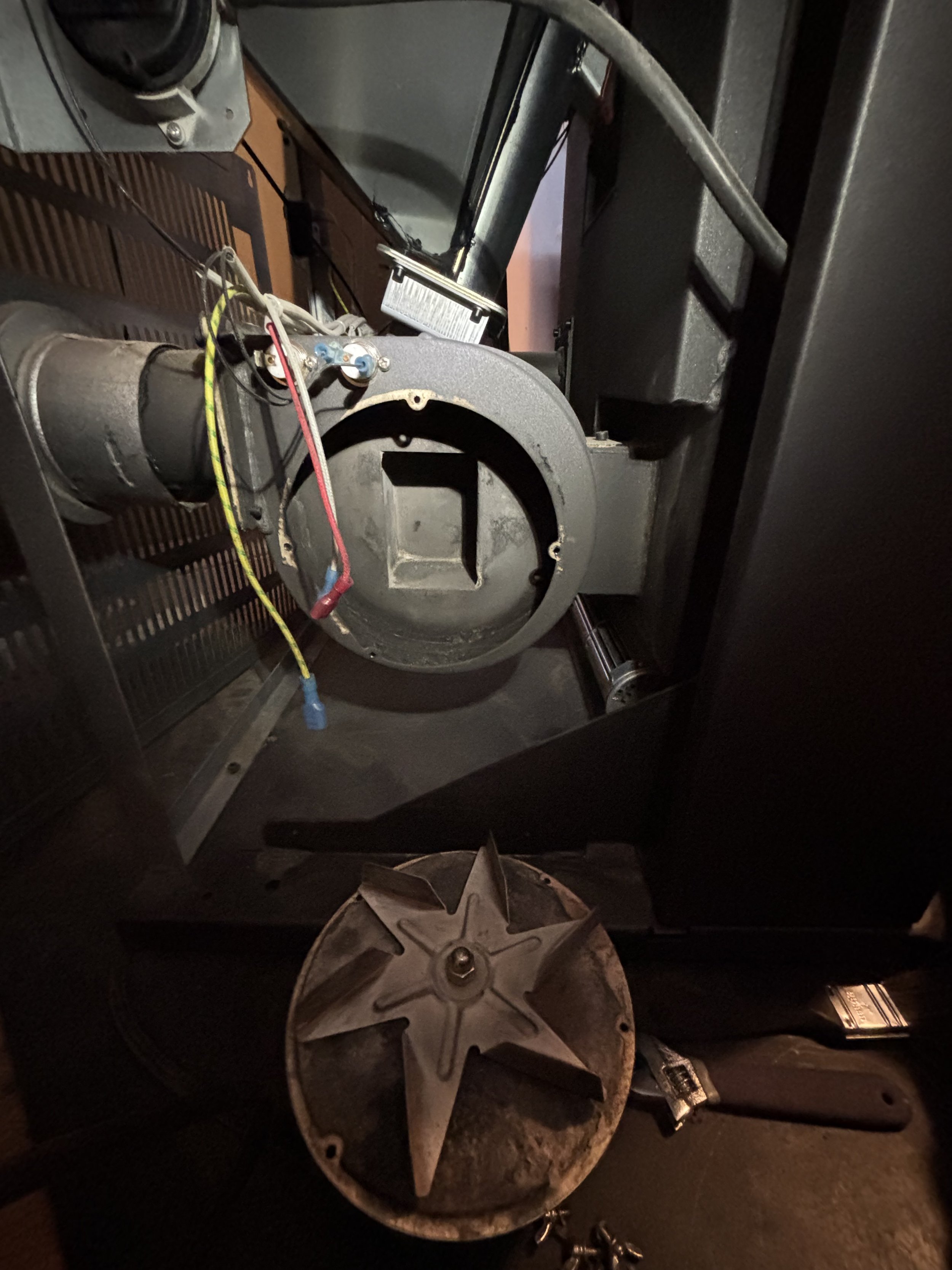 Interior of an arcade or pinball machine showing a large metal spinning disk and a cylindrical component with wires, screws, and a metal star-shaped spinner on a work surface.