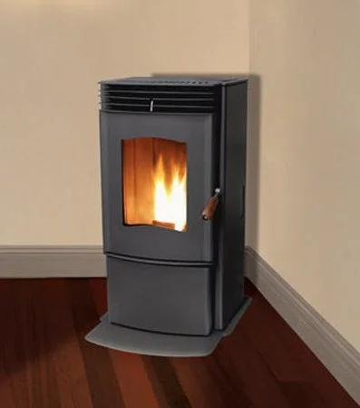 A freestanding pellet stove with a fire burning inside, placed in the corner of a room on a wooden floor with beige walls.