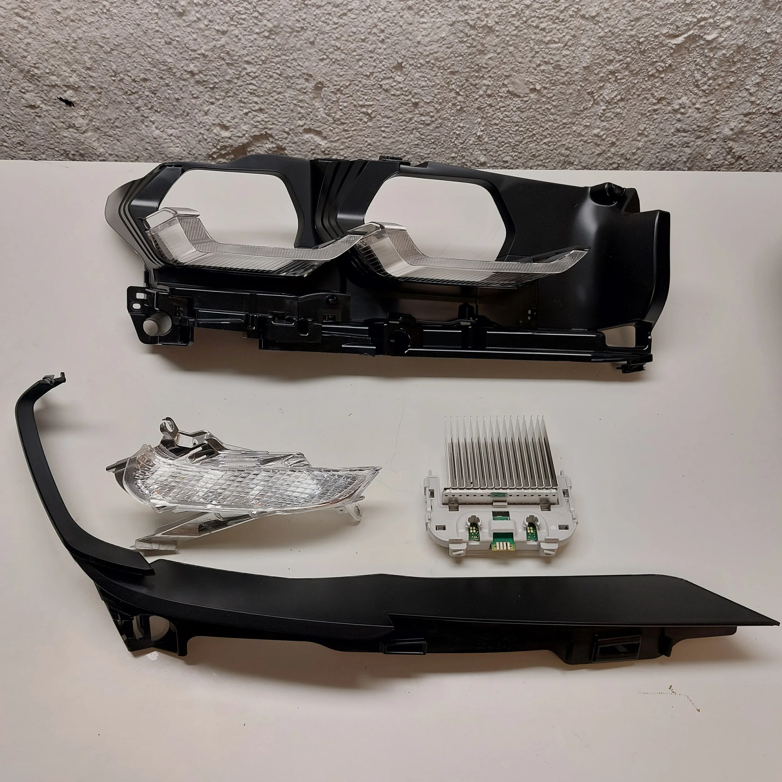 Disassembled BMW G30 headlight components including black plastic housing, clear lens covers, and a white electronic module with fins.