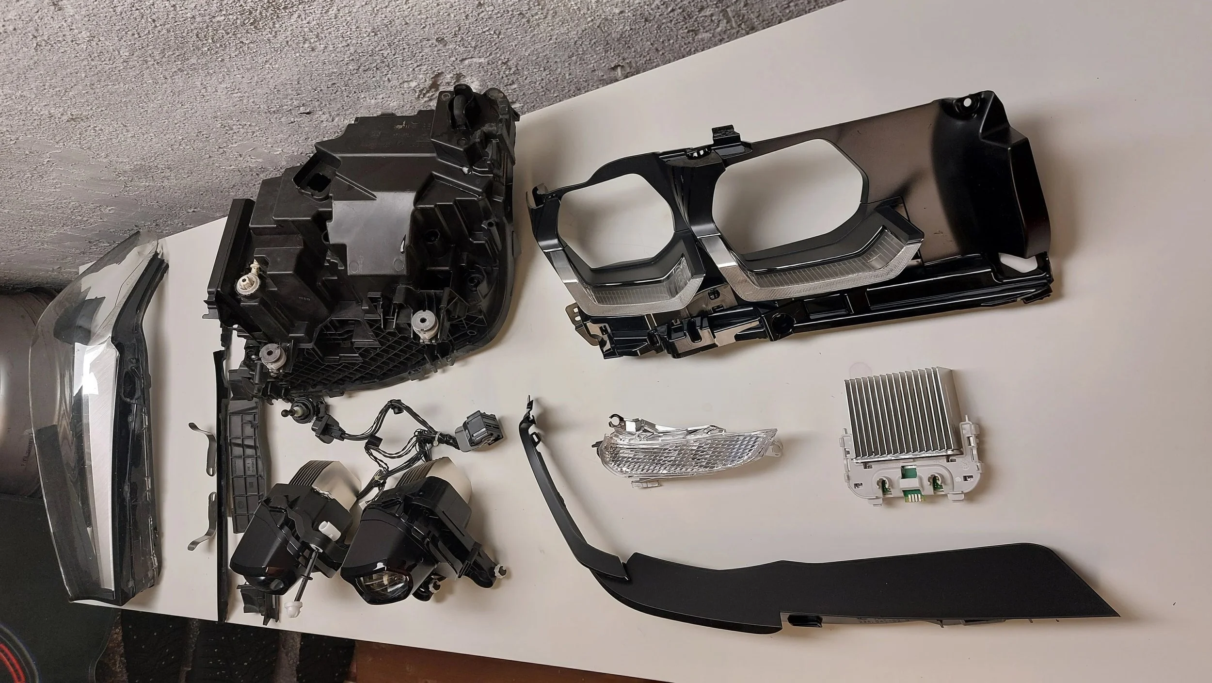 Disassembled car headlight components laid out on a white surface, including parts like the headlight housing, control modules, wiring, and lens.