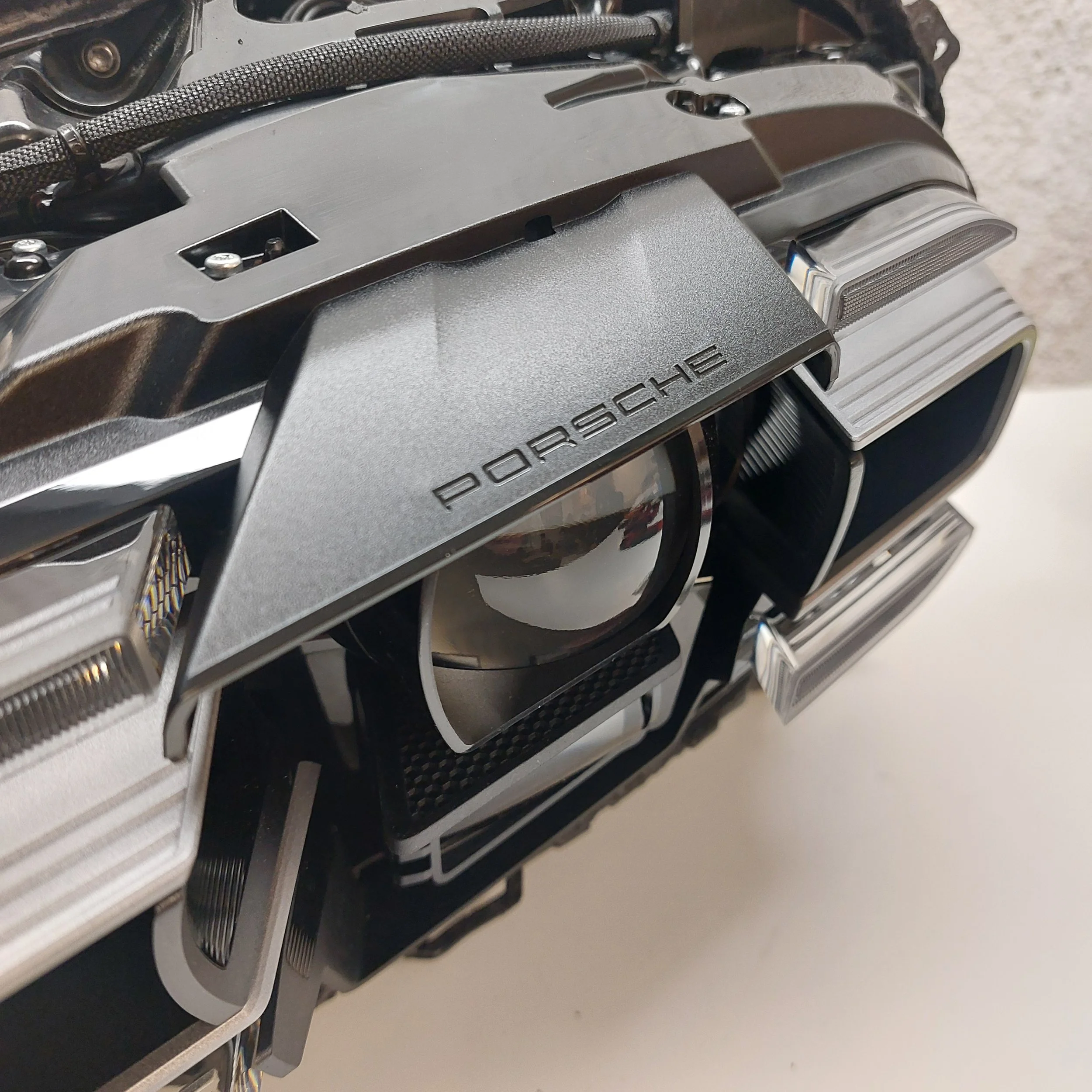 Close-up of a modern Porsche car headlight with the Porsche logo on the black housing surrounding the headlights.