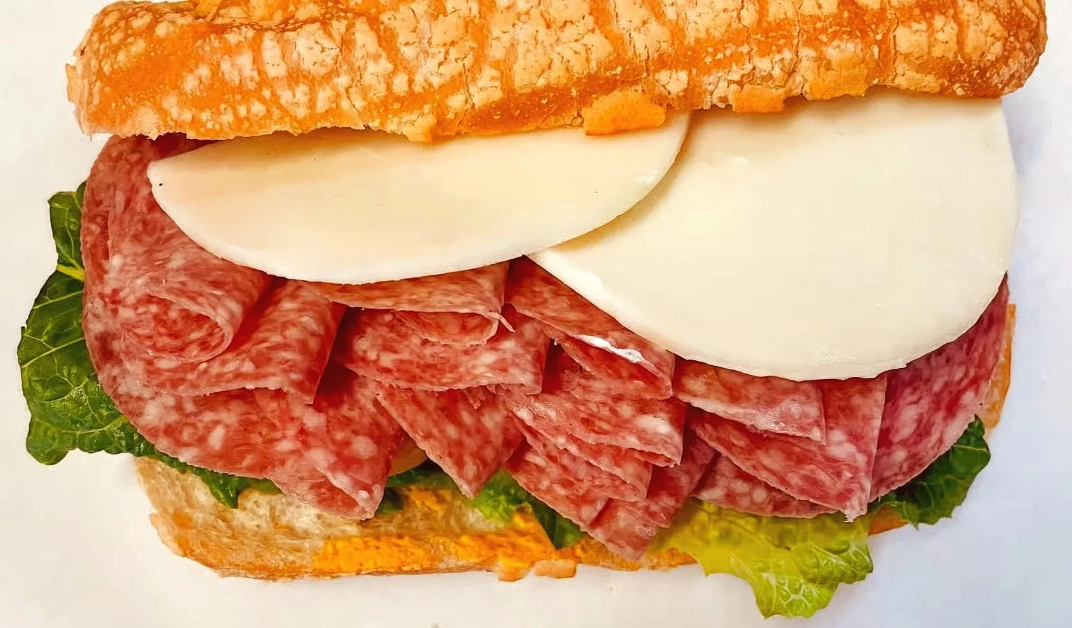 Close-up of a sandwich with layers of lettuce, sliced salami, mozzarella cheese, and a toasted hoagie bun.