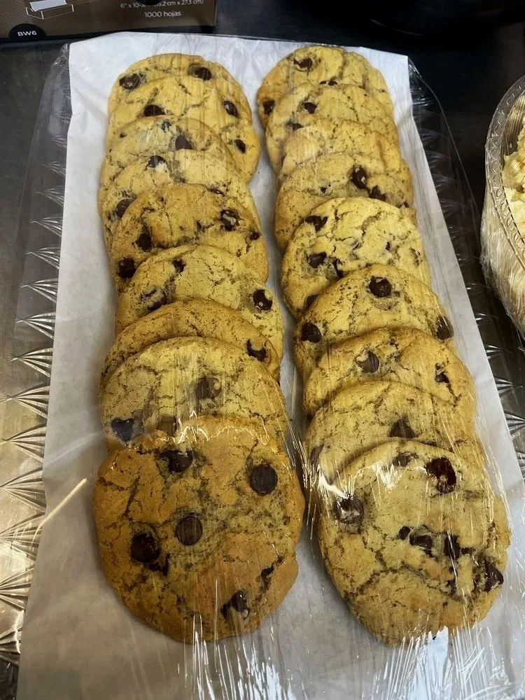 A tray of chocolate chip cookies on parchment paper covered with plastic wrap.
