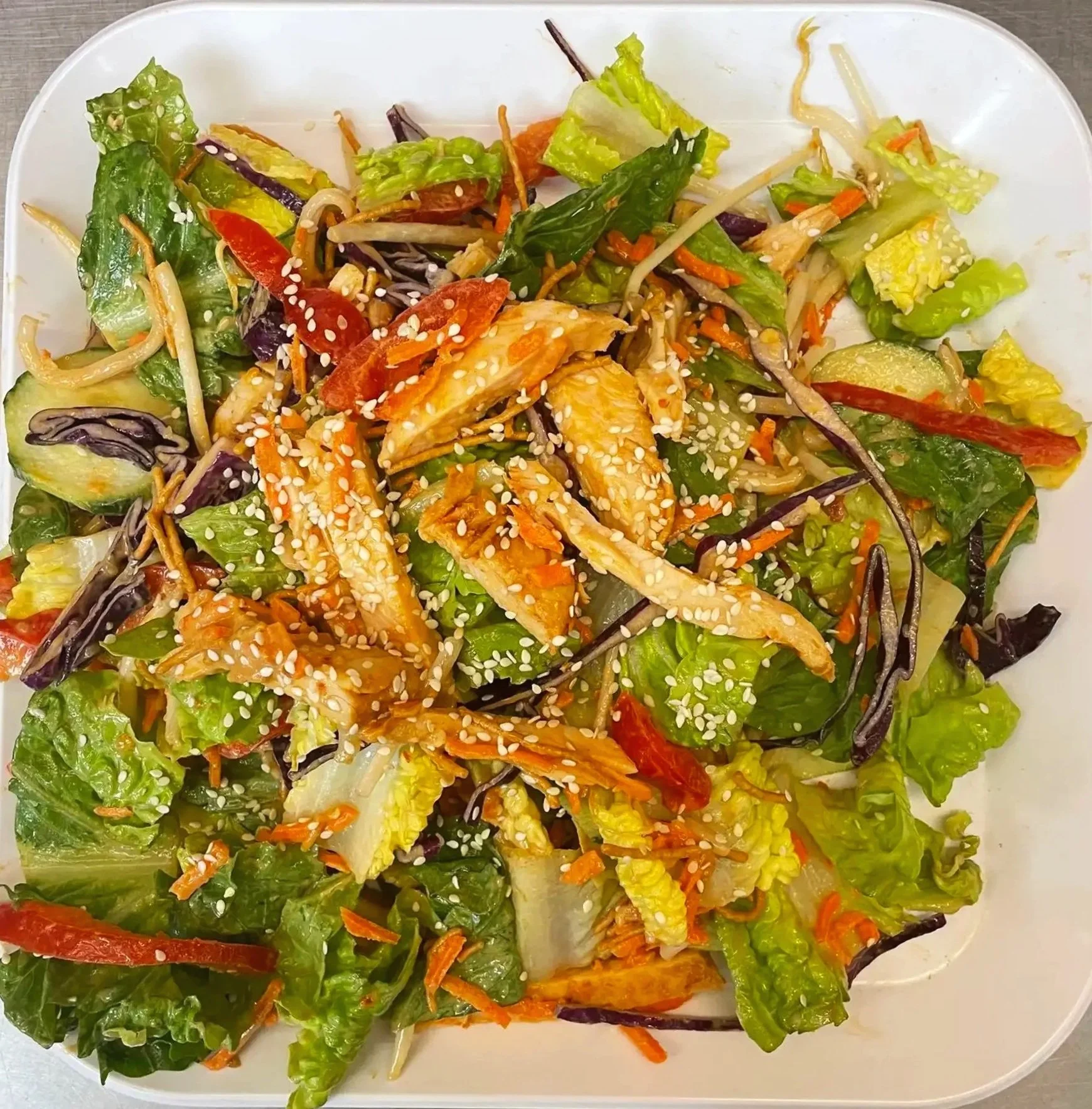 Mixed salad with lettuce, cucumbers, red peppers, shredded carrots, bean sprouts, and sprinkled sesame seeds.