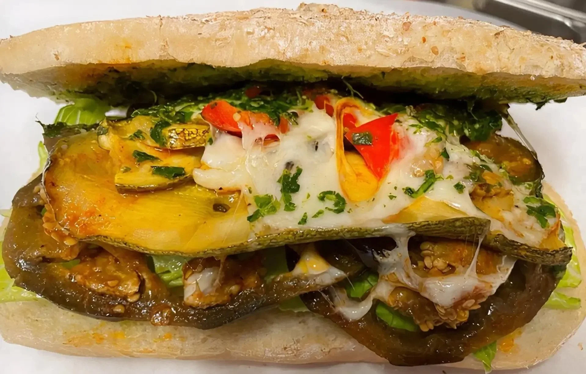 Open face sandwich with roasted vegetables, melted cheese, and chopped herbs served on toasted bread.