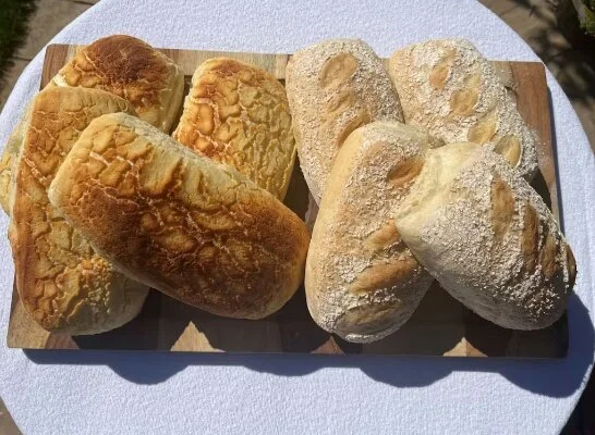 Six pieces of bread on a wooden serving tray, with three pieces of bread that are golden brown and three pieces that are light beige with flour dusting.