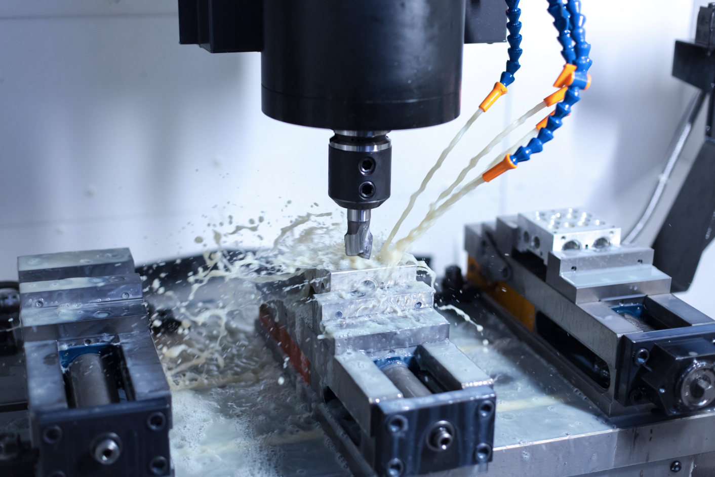 A CNC milling machine cutting into a metal workpiece with coolant spray in a manufacturing environment.