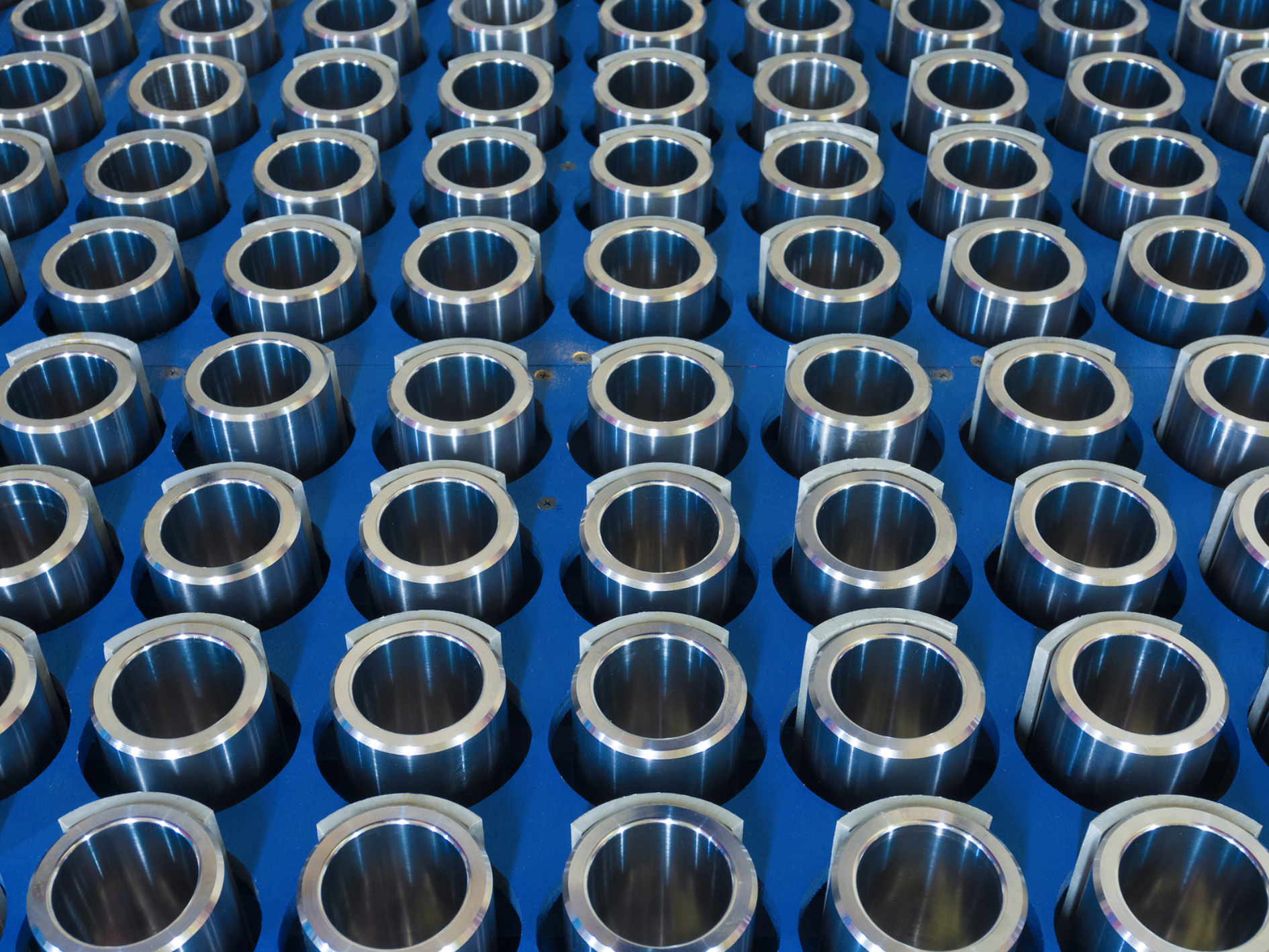 Multiple cylindrical metal components arranged in rows on a blue surface.