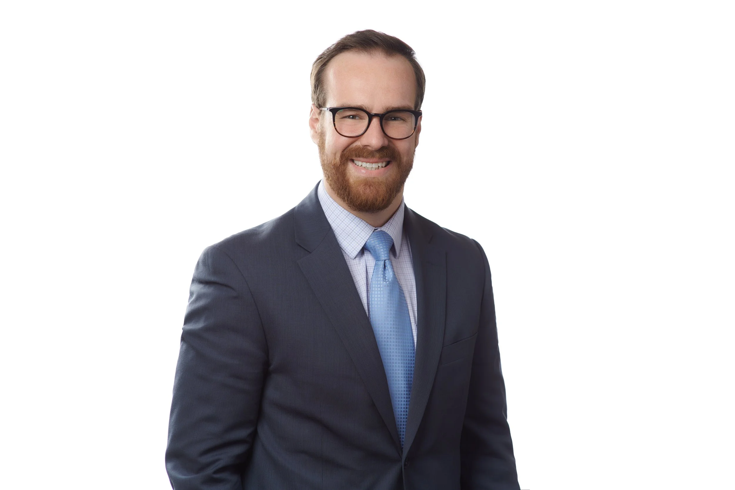 A professional man wearing glasses and a dark suit with a light blue tie, smiling against a plain white background.