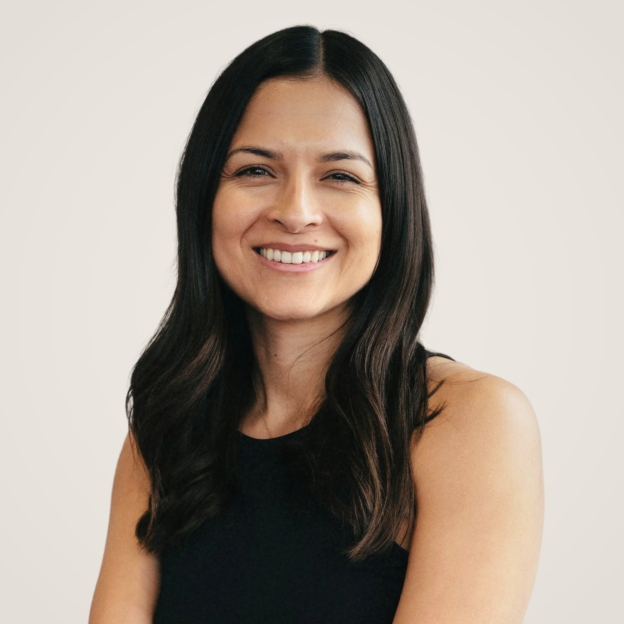 A woman with long dark hair smiling, wearing a sleeveless black top, against a plain white background.