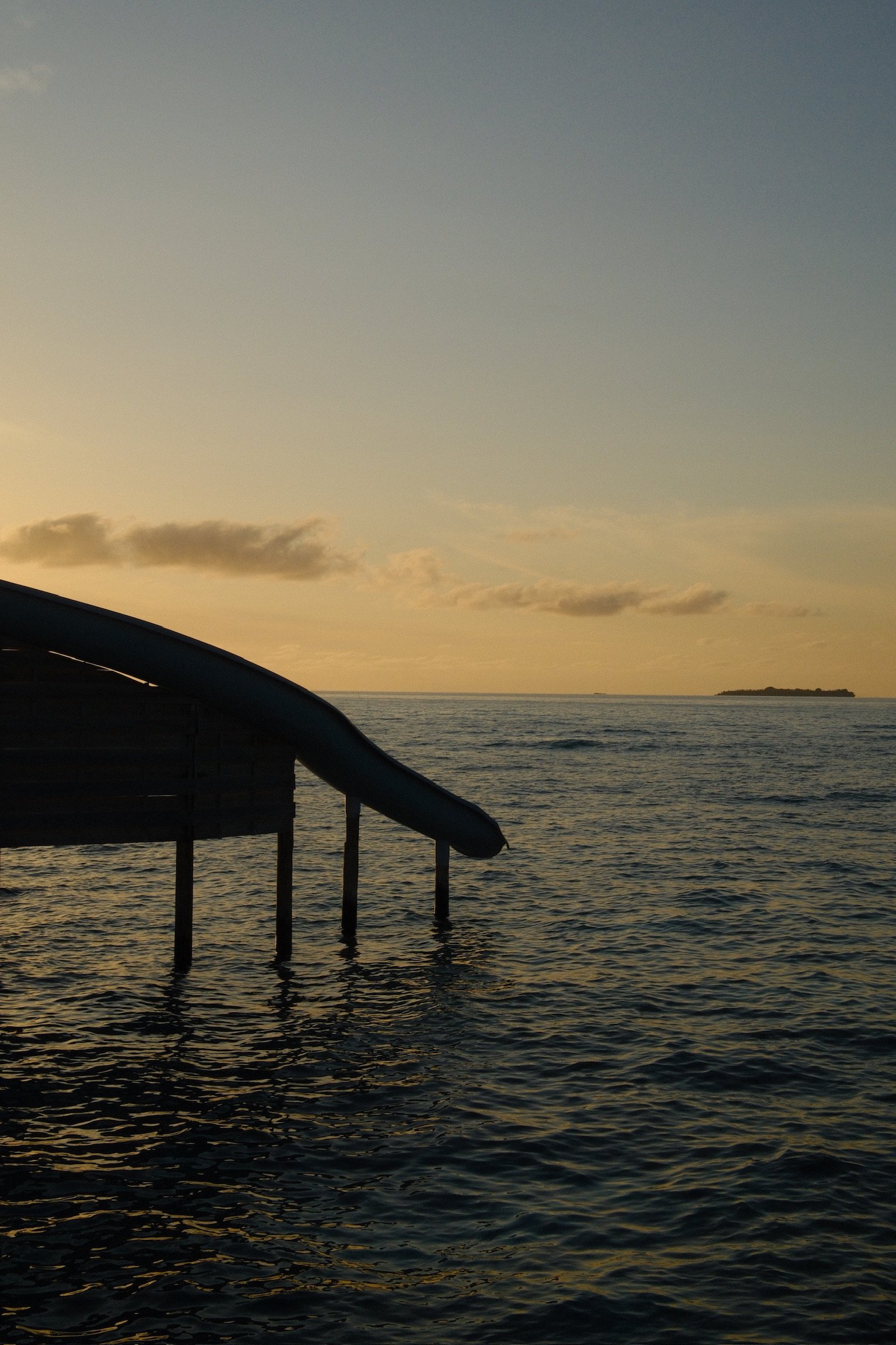 Overwater slide at Soneva Fushi in the Maldives at sunset, with the ocean and island silhouettes in the distance.