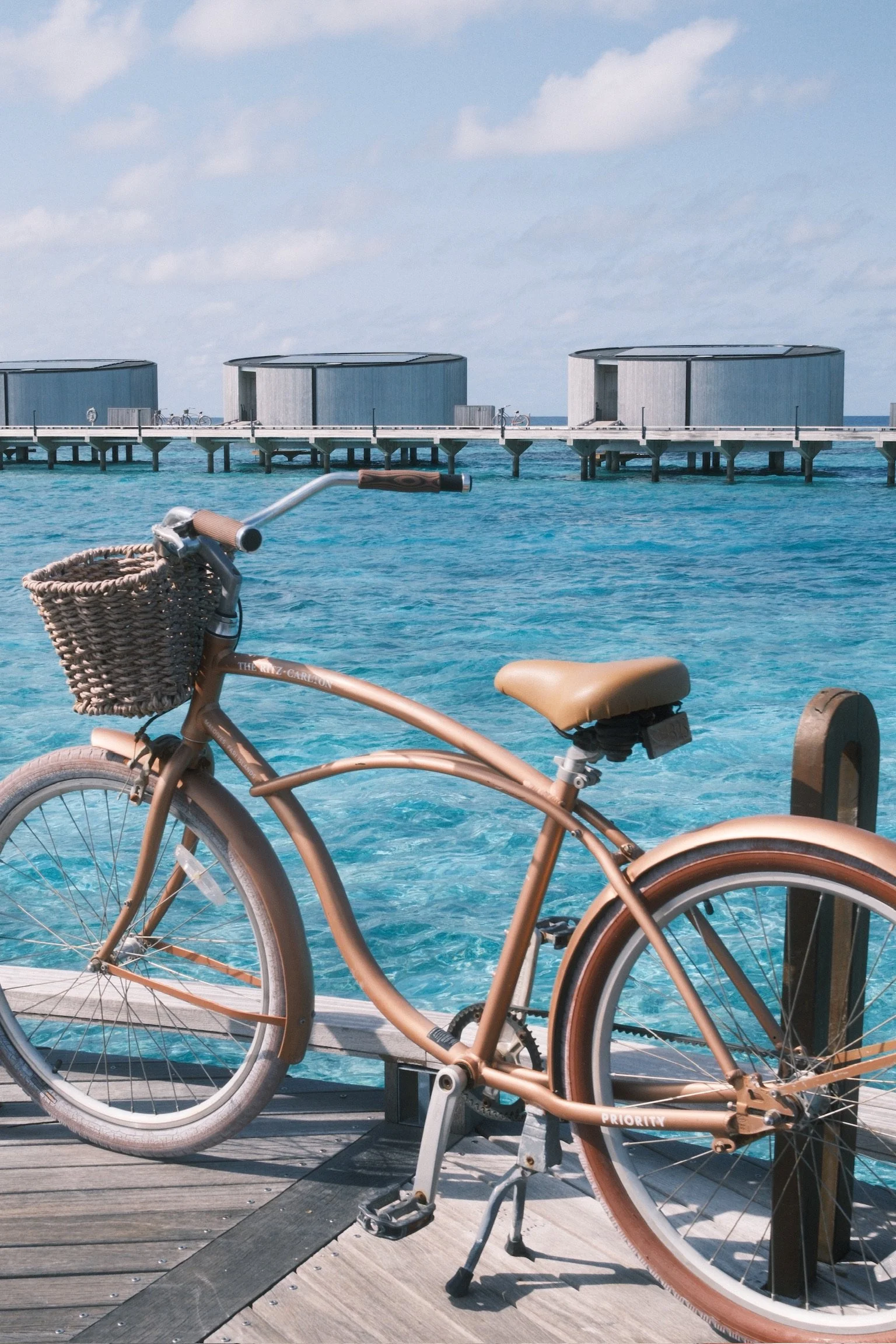 A bicycle with a front basket is parked on a wooden jetty at Ritz Carlton Maldives