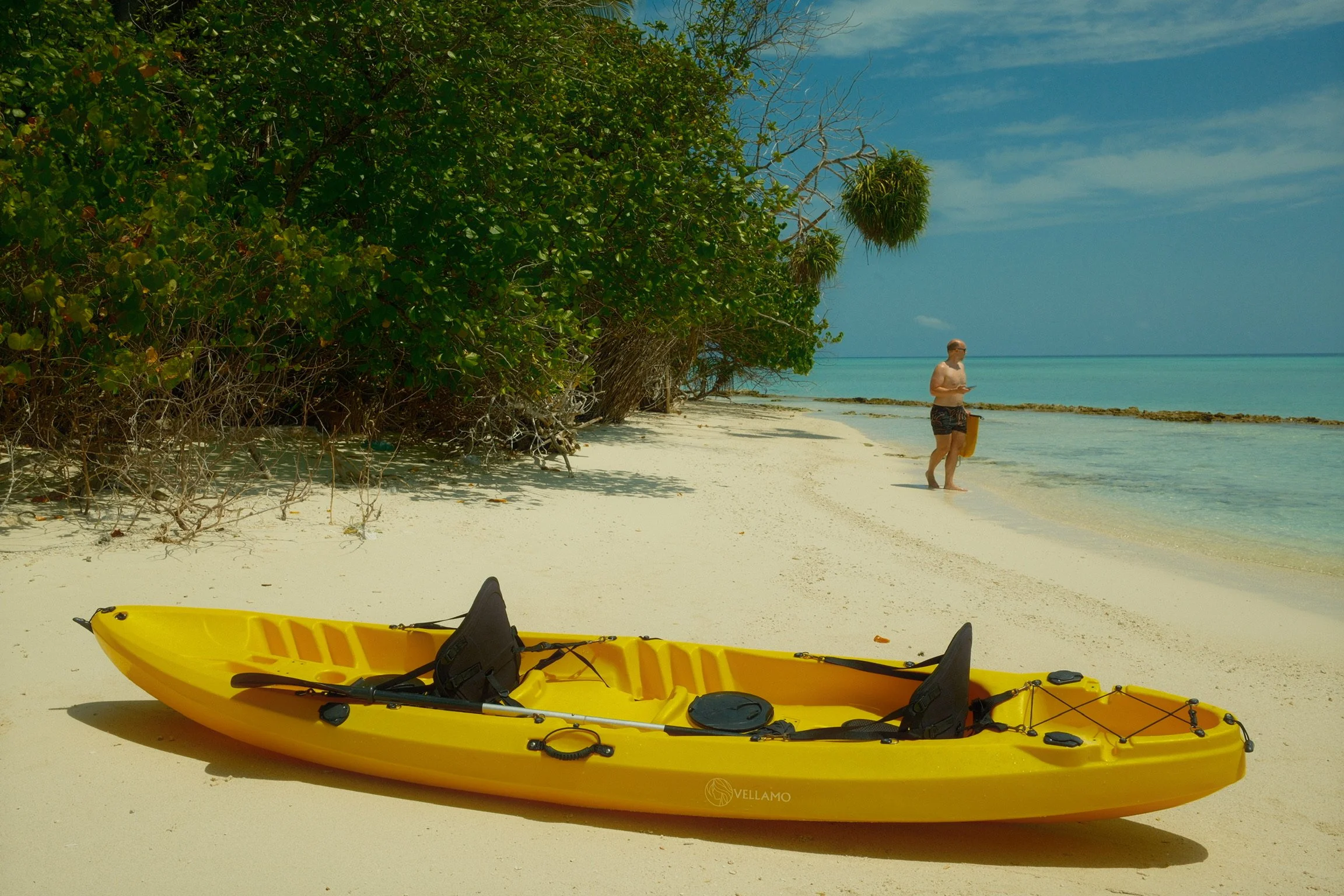 Matt on a white sand beach in the Maldives after kayaking, with a yellow kayak beside the turquoise lagoon.