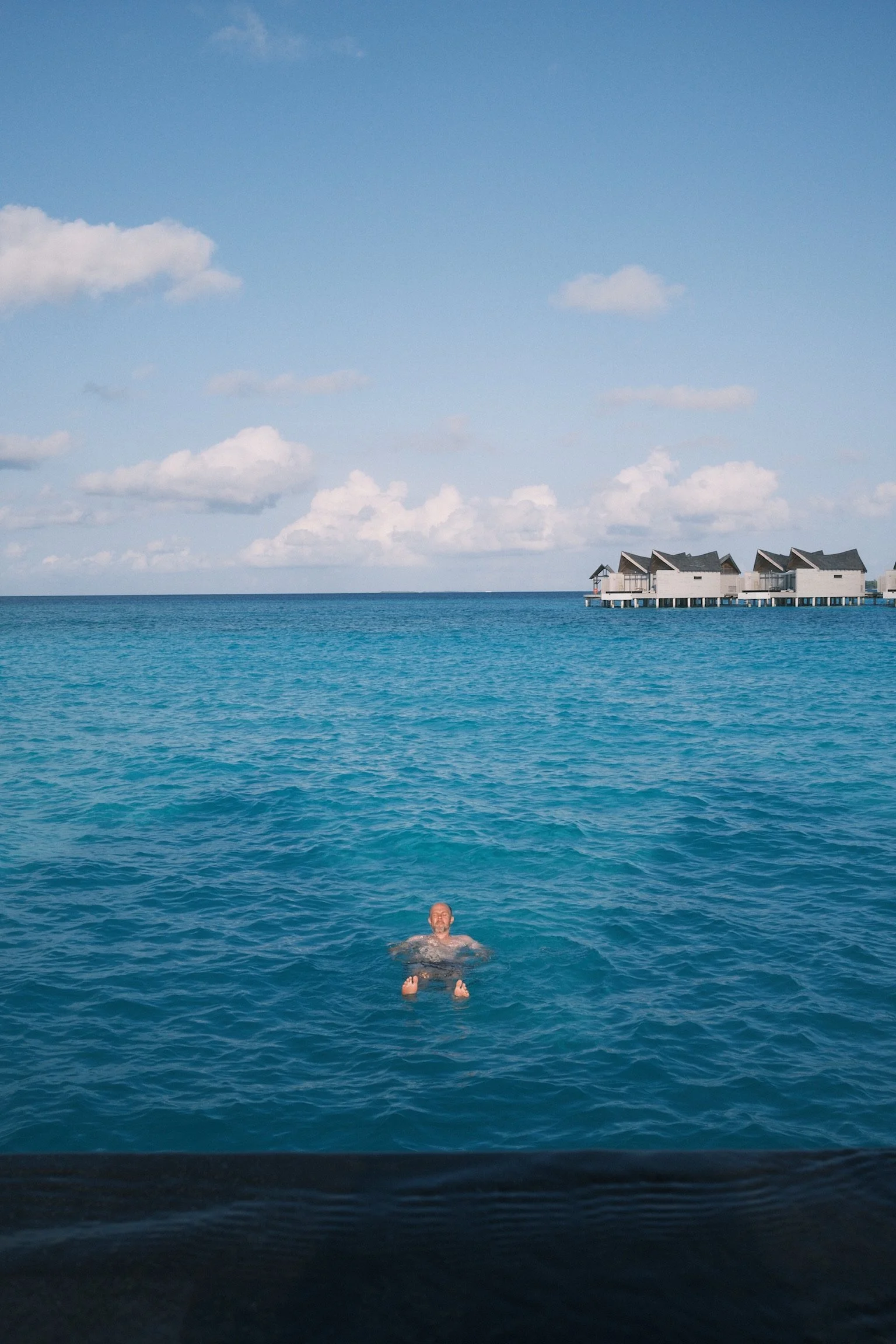 Matt floating in the clear ocean with a row of overwater villas in the distance.