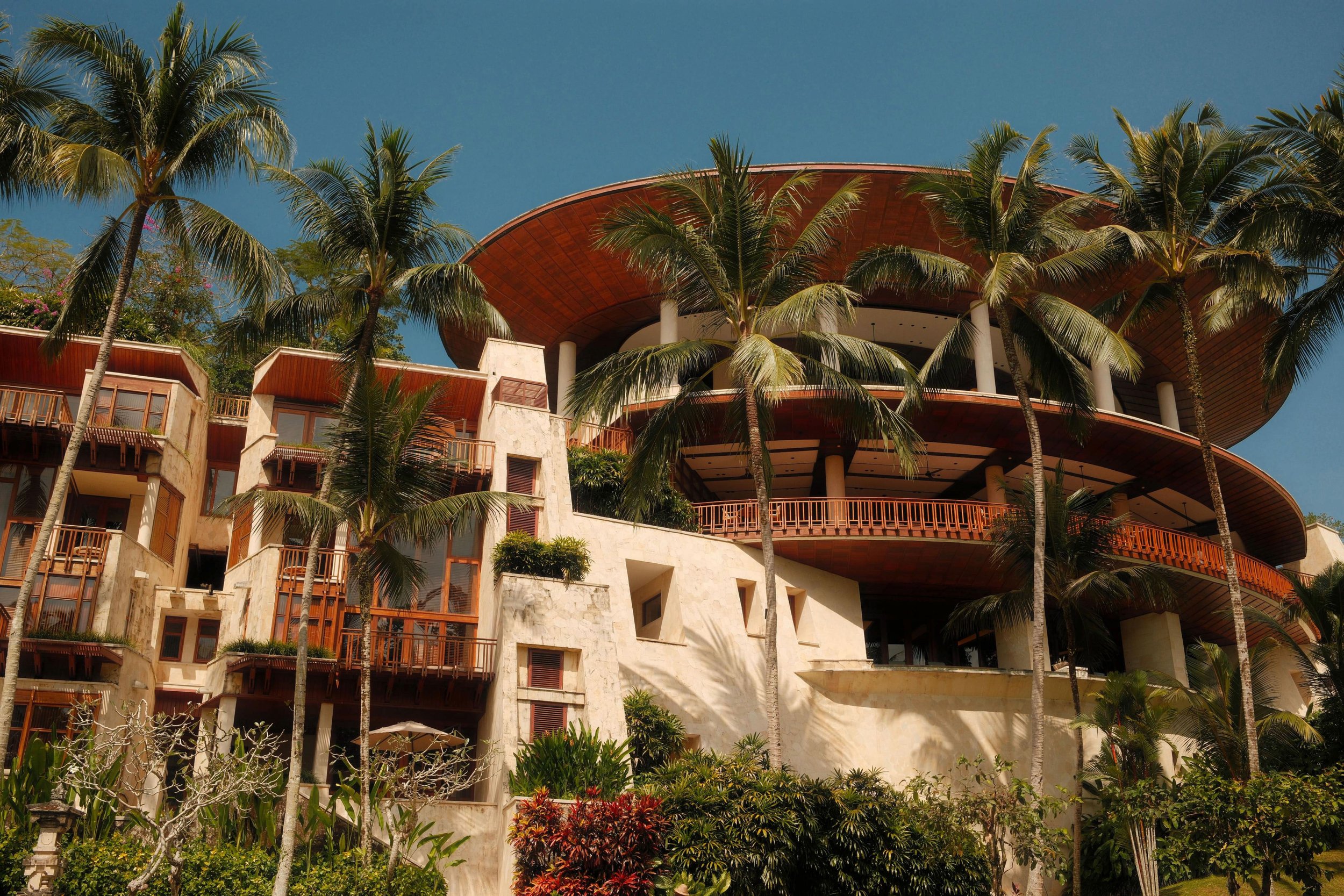 The curved, multi-level main building at Four Seasons Resort Bali at Sayan rising above palm trees and tropical gardens.