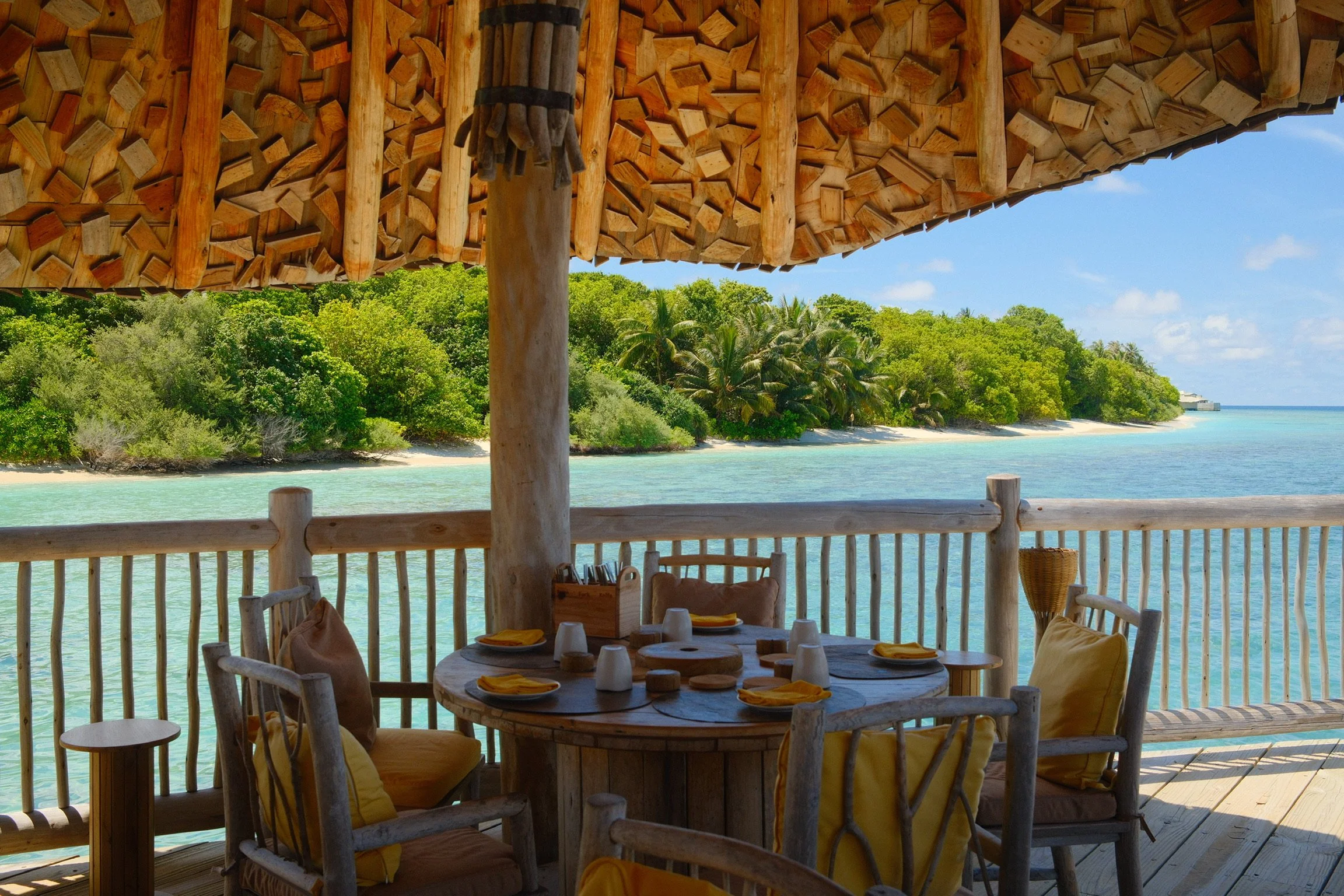 Outdoor dining table on a wooden deck at Soneva Fushi in the Maldives, overlooking turquoise water and a palm-fringed island.