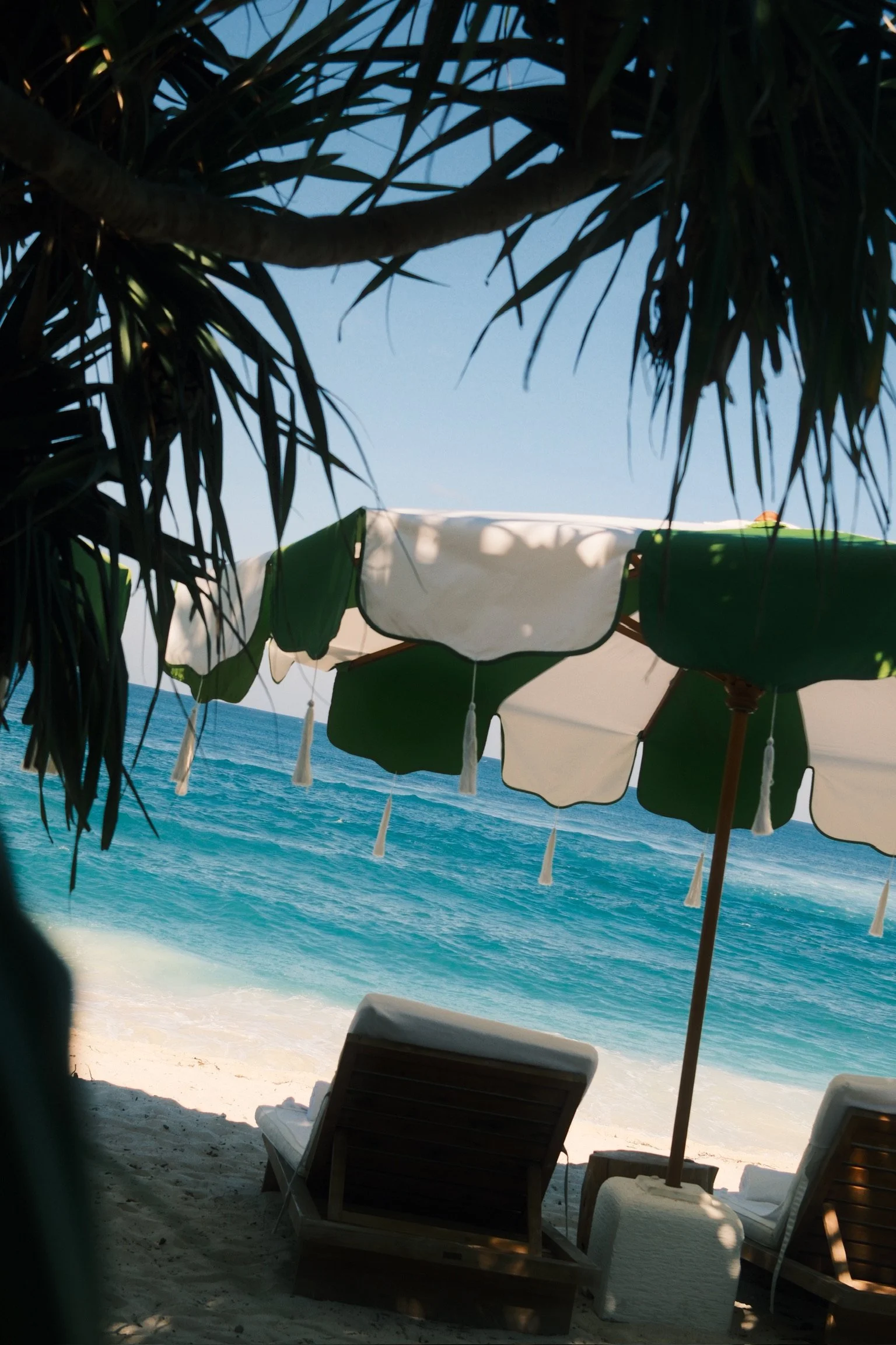 Green-and-white parasols shading wooden sun loungers beside NIHI Rote’s turquoise shoreline.
