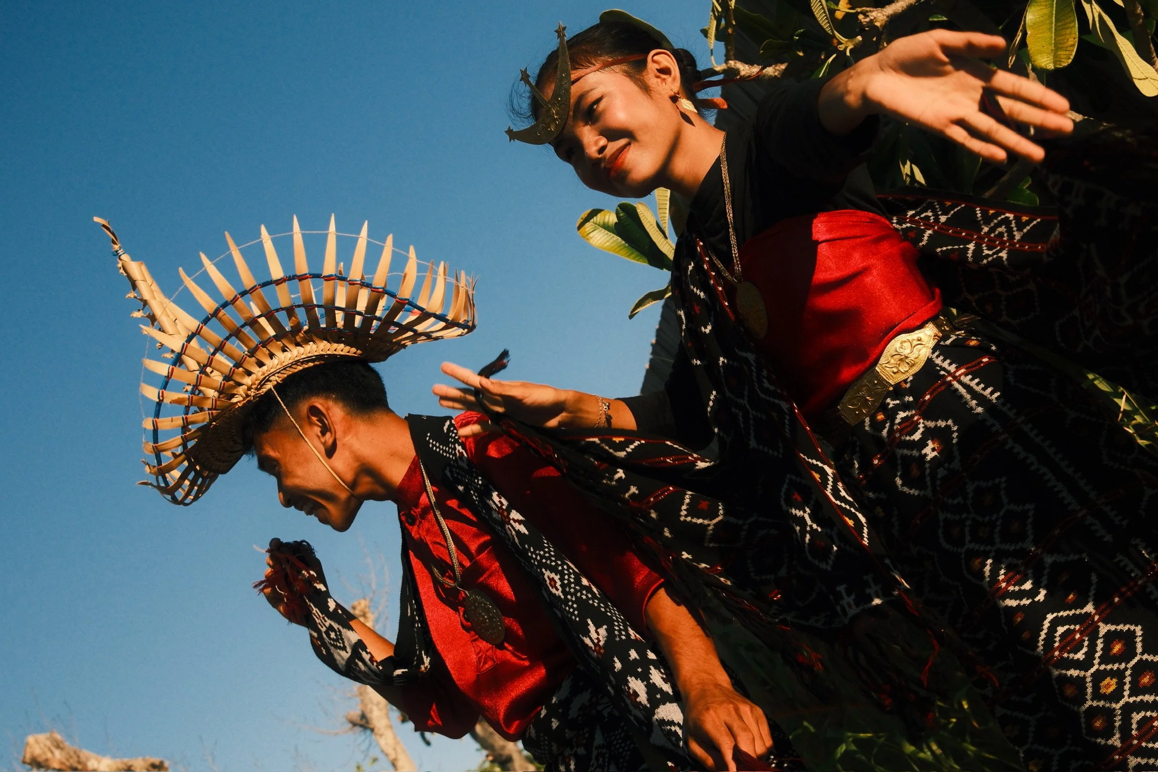 Two Rotenese dancers performing outdoors in patterned ceremonial clothing and handcrafted headdresses.