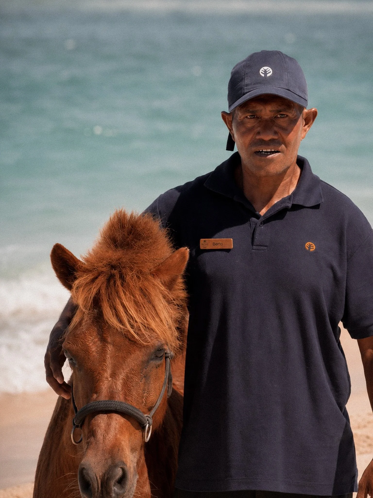 A NIHI Rote horse handler standing beside a small chestnut horse on the beach.