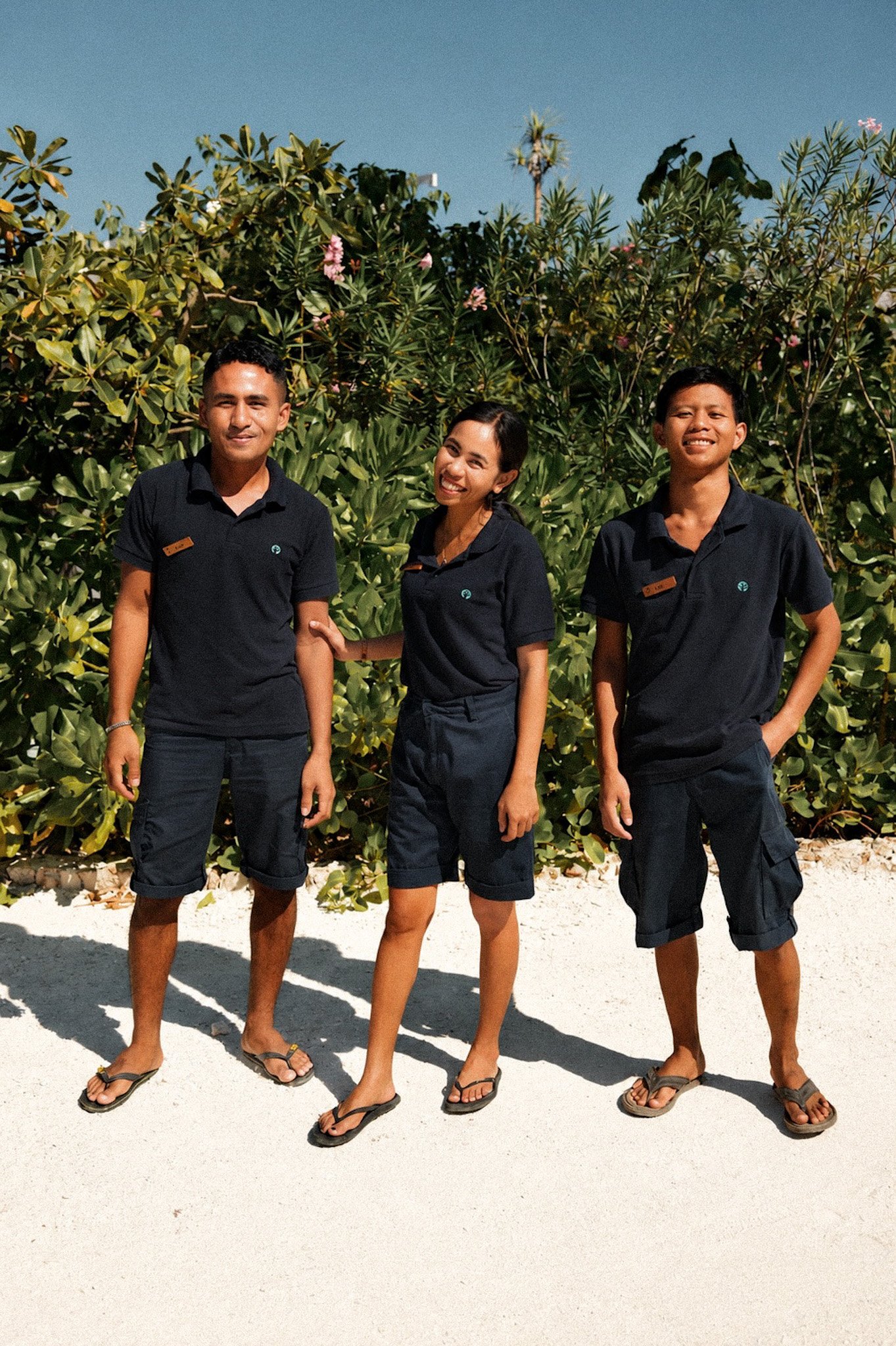 Three smiling NIHI Rote hosts standing together in front of tropical greenery.