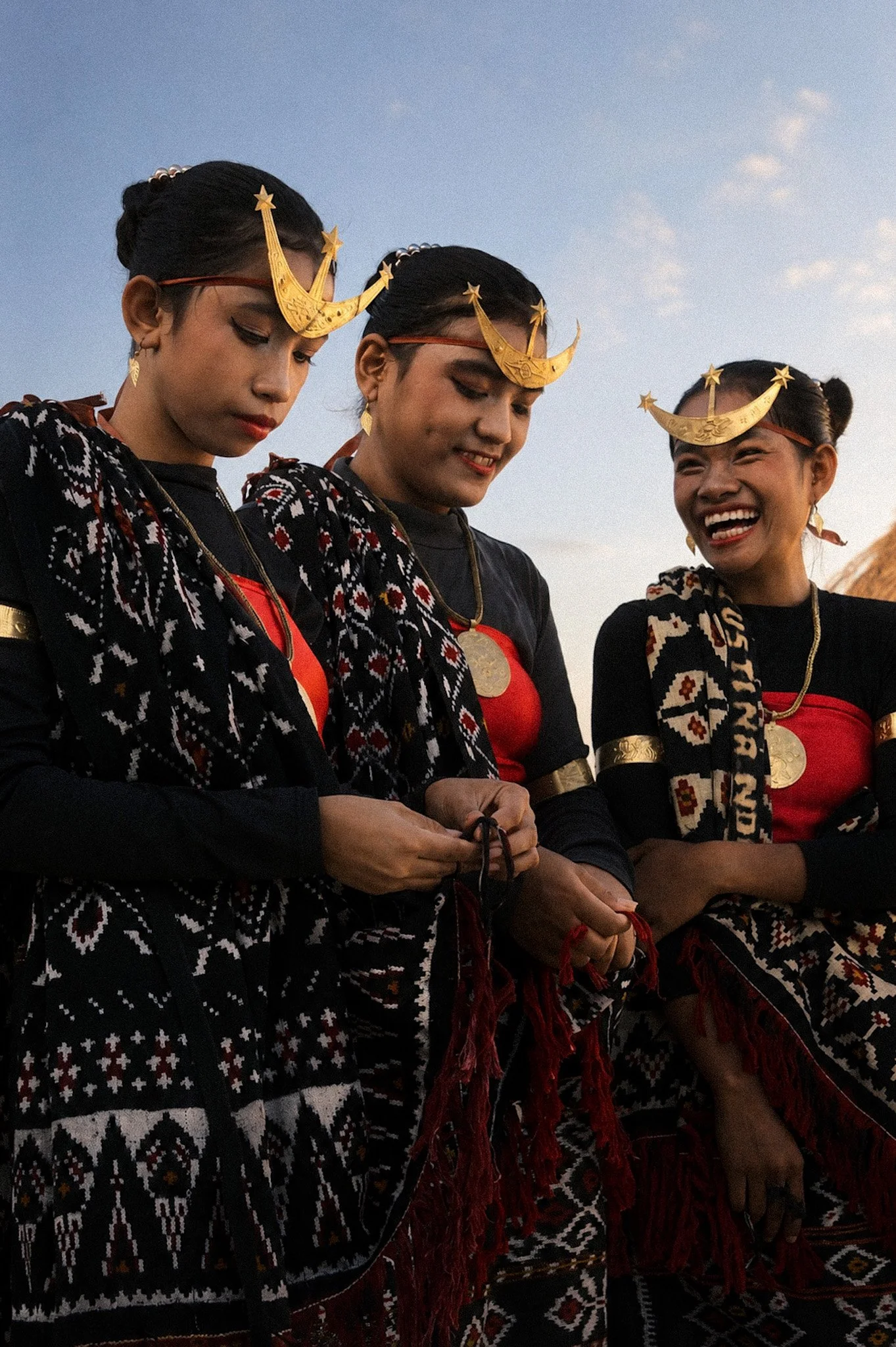 Three Rotenese performers wearing patterned textiles, gold jewellery and traditional crescent-shaped headdresses.