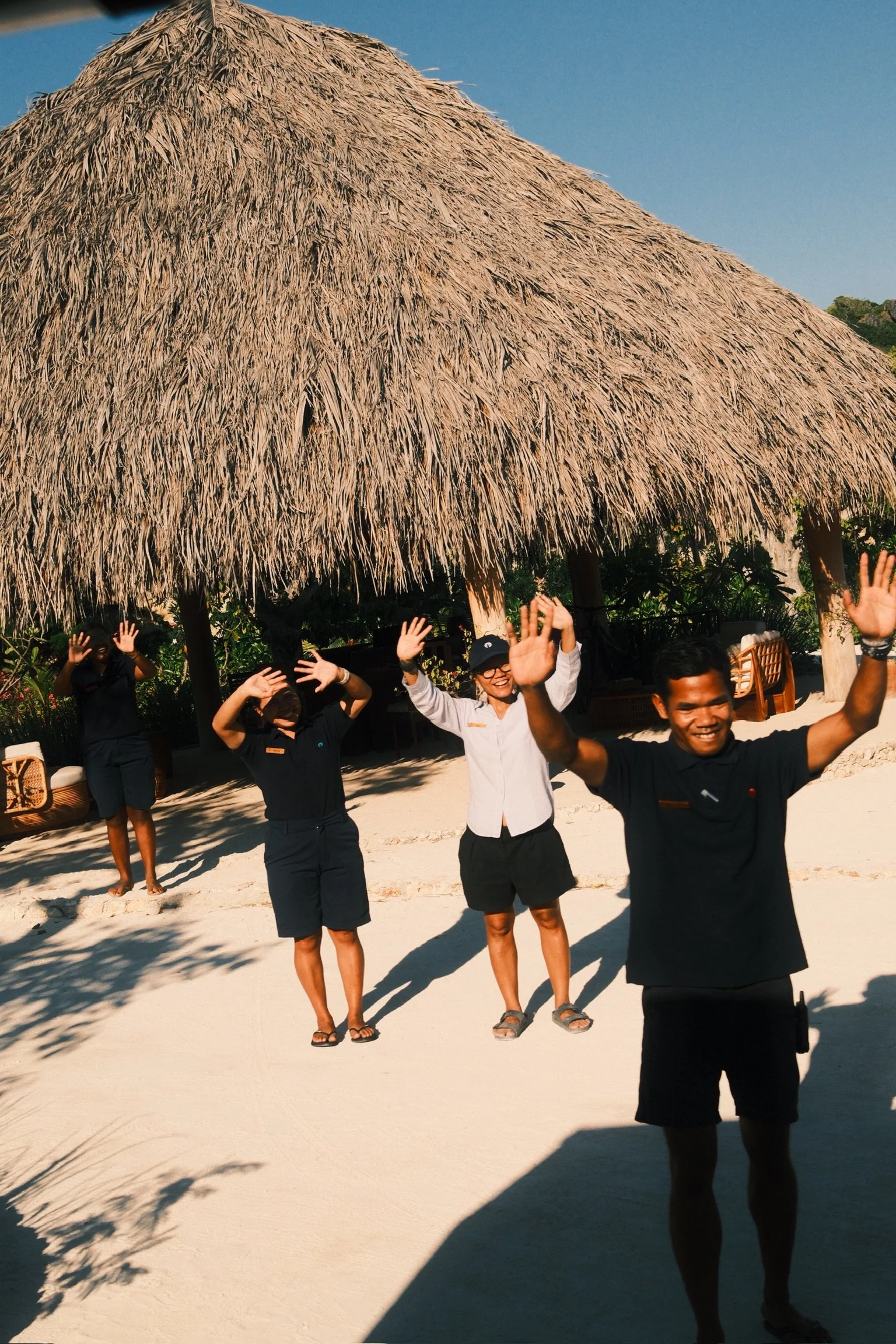 Members of the NIHI Rote team smiling and waving goodbye beneath a thatched roof.