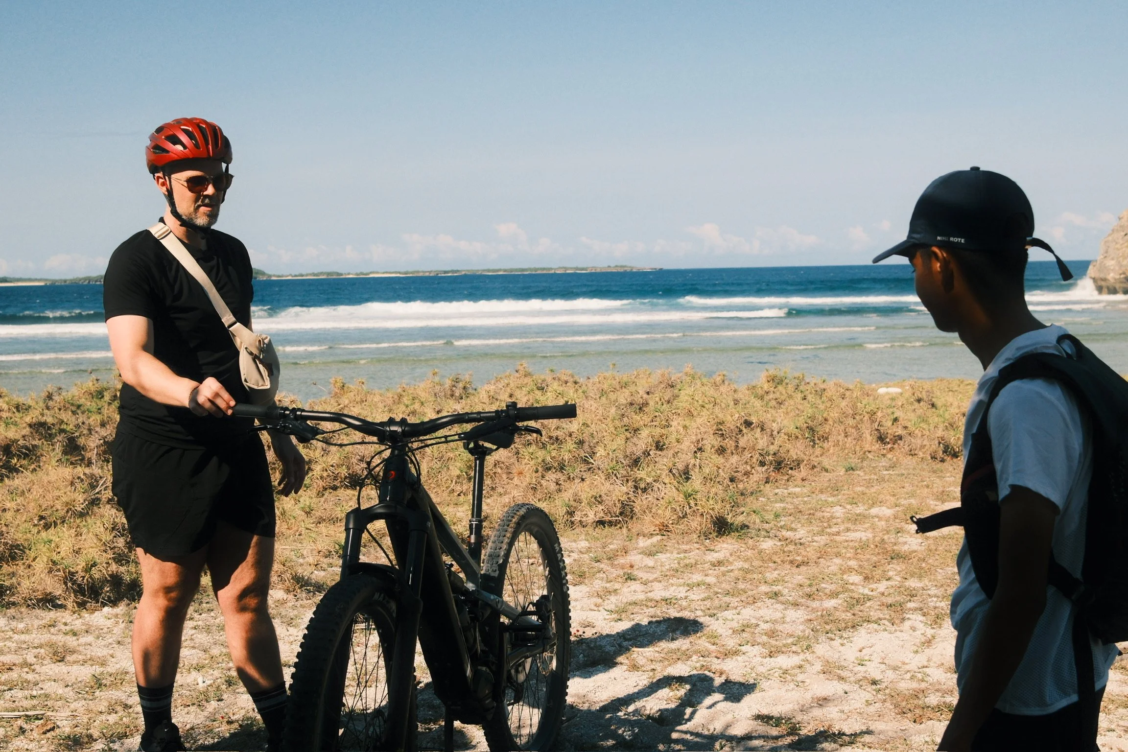Matt standing with a mountain bike and a NIHI Rote guide beside the ocean.