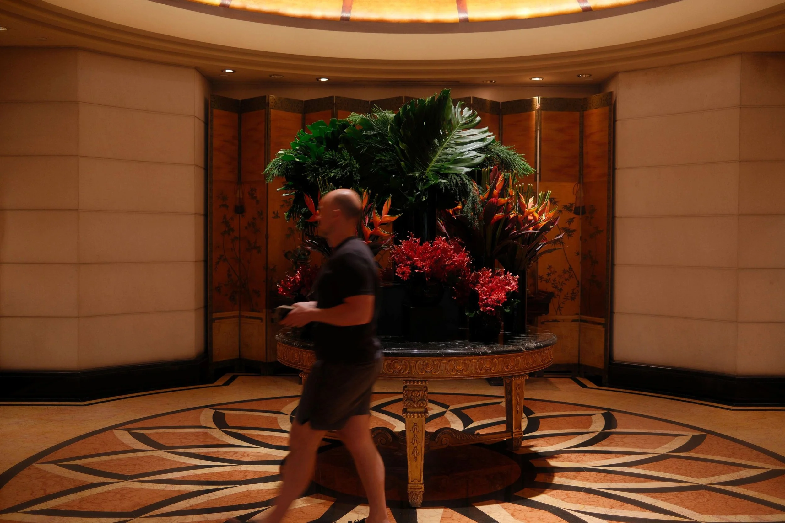 Matt passing a large arrangement of tropical leaves and red flowers in the lobby of Four Seasons Hotel Singapore.