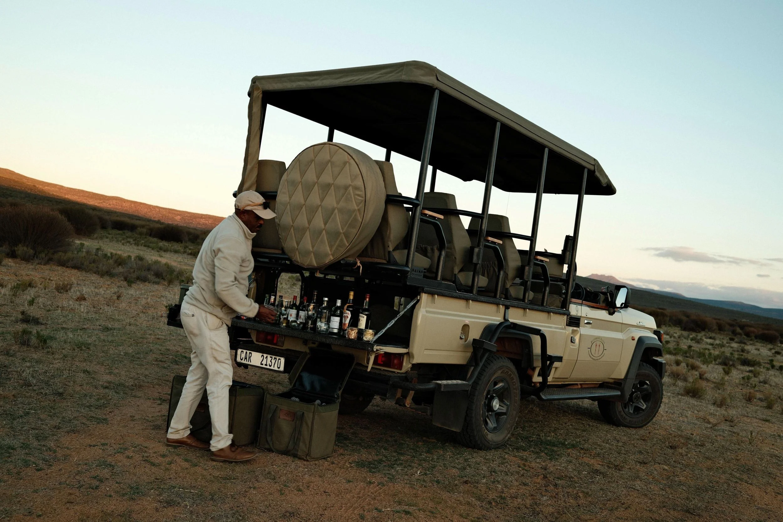 A Bushmans Kloof guide arranging sundowner drinks at the back of an open safari vehicle.