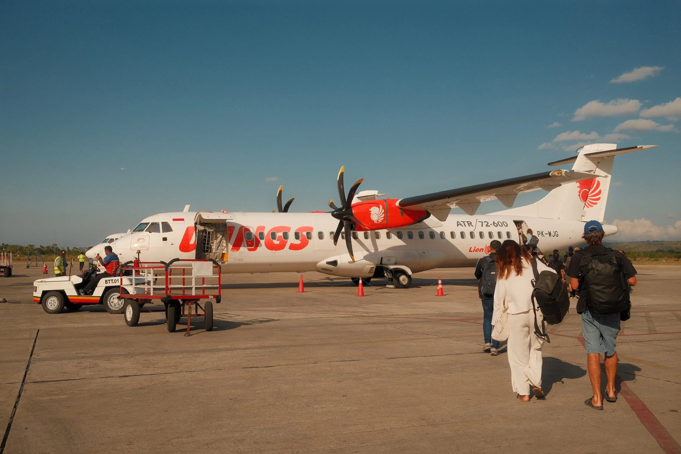Passengers walking across the airport tarmac towards a Wings Air turboprop aircraft.