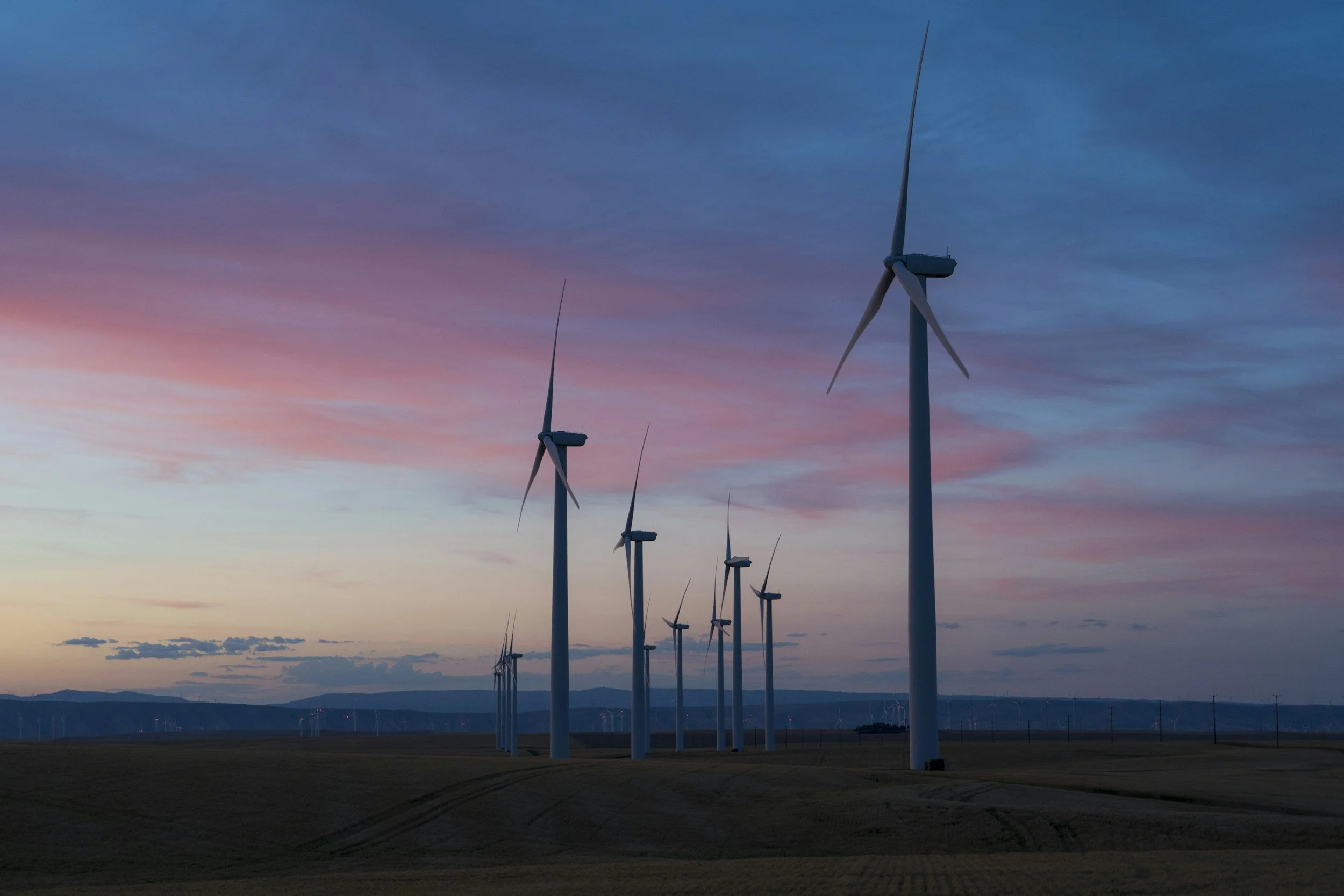 A row of wind turbines in a landscape during sunset with pink and blue sky.