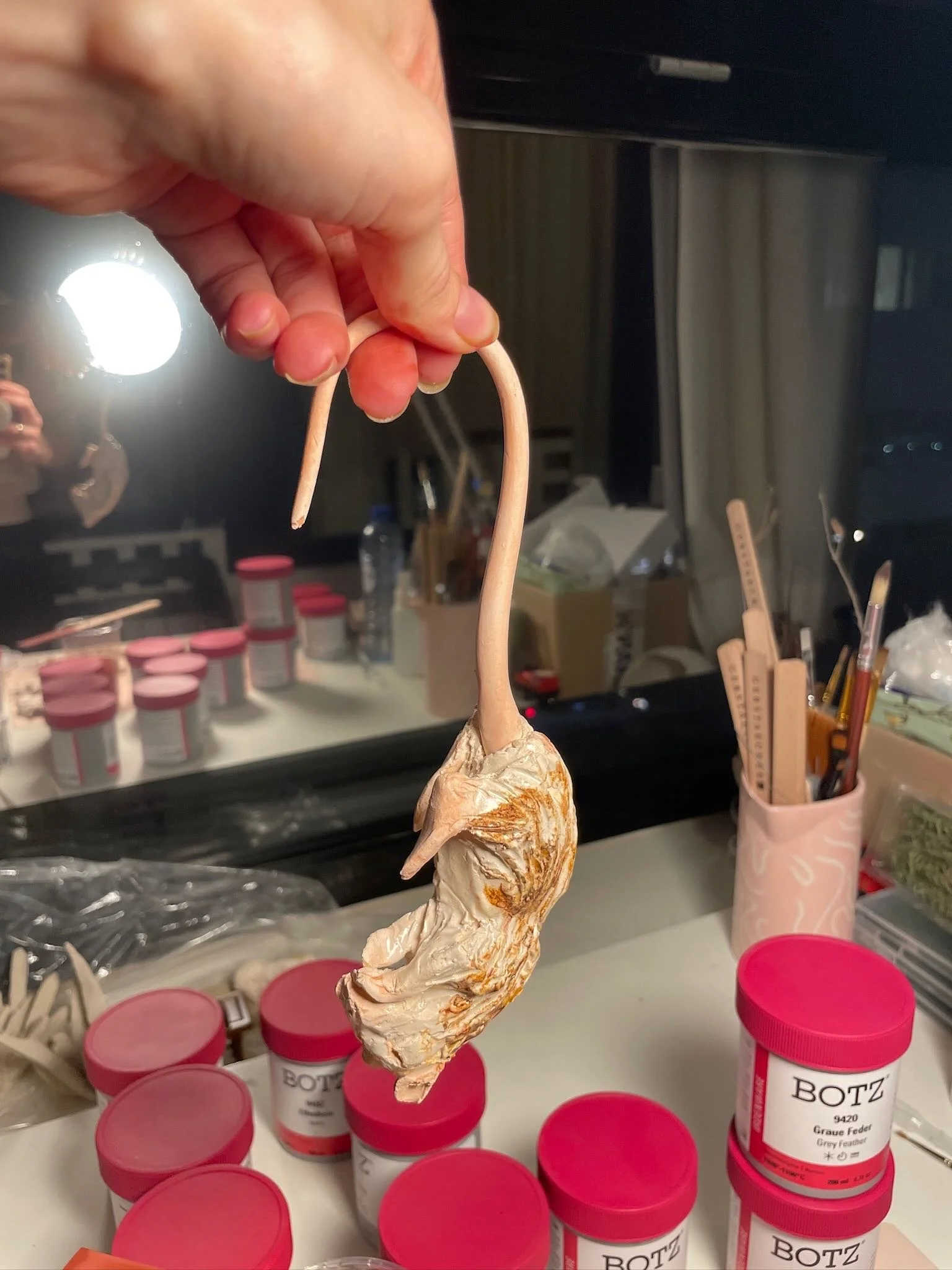 Person holding a ceramic rat with a long, thin tail with white and brown glaze