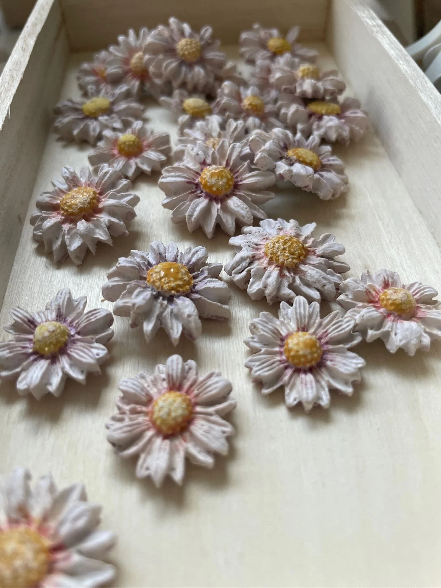Decorative miniature flower-shaped items with pinkish petals and yellow centers arranged on a light-colored wooden tray.