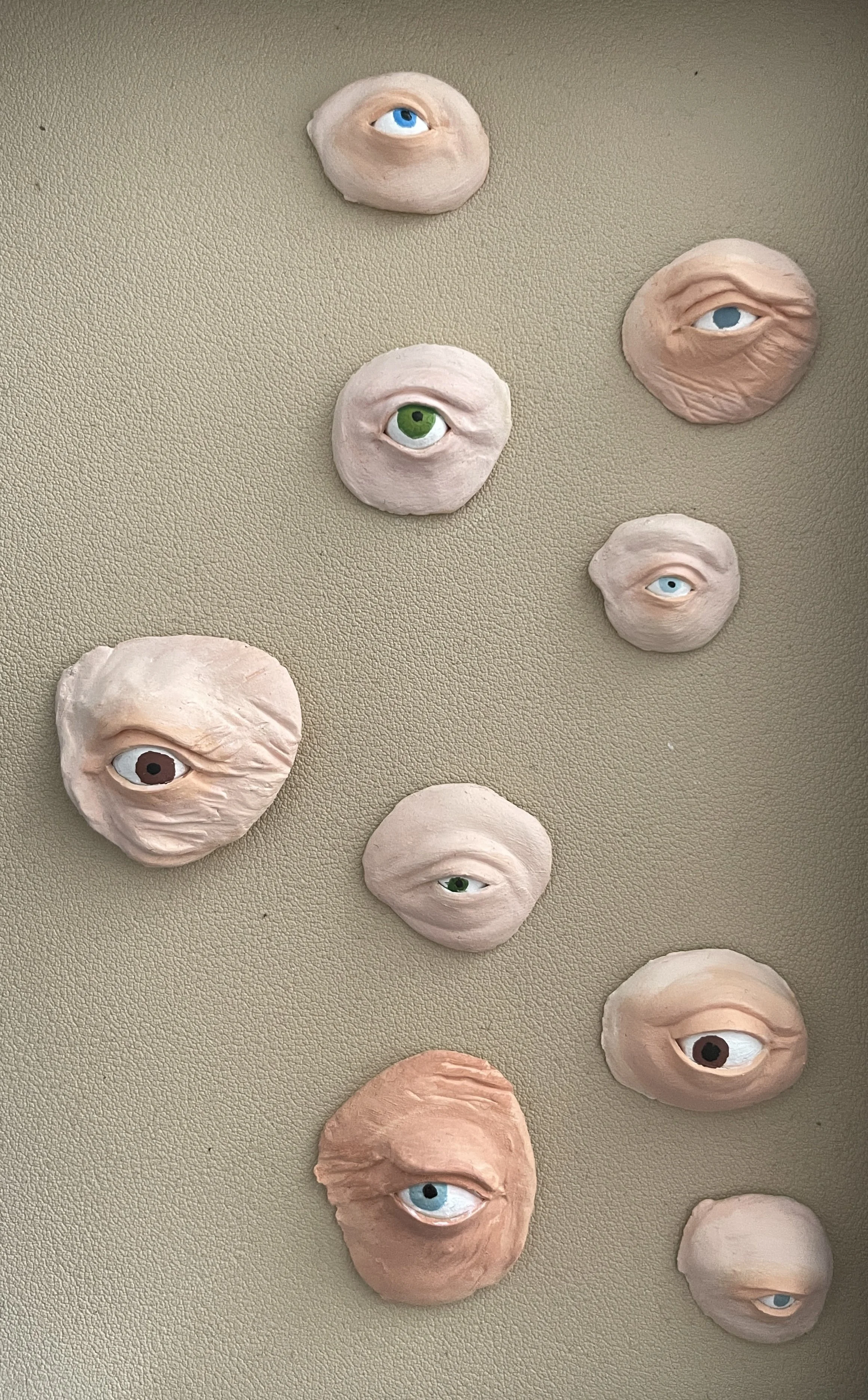 Various painted clay or ceramic sculptures of human eyes with different colors and textures, arranged on a flat surface.