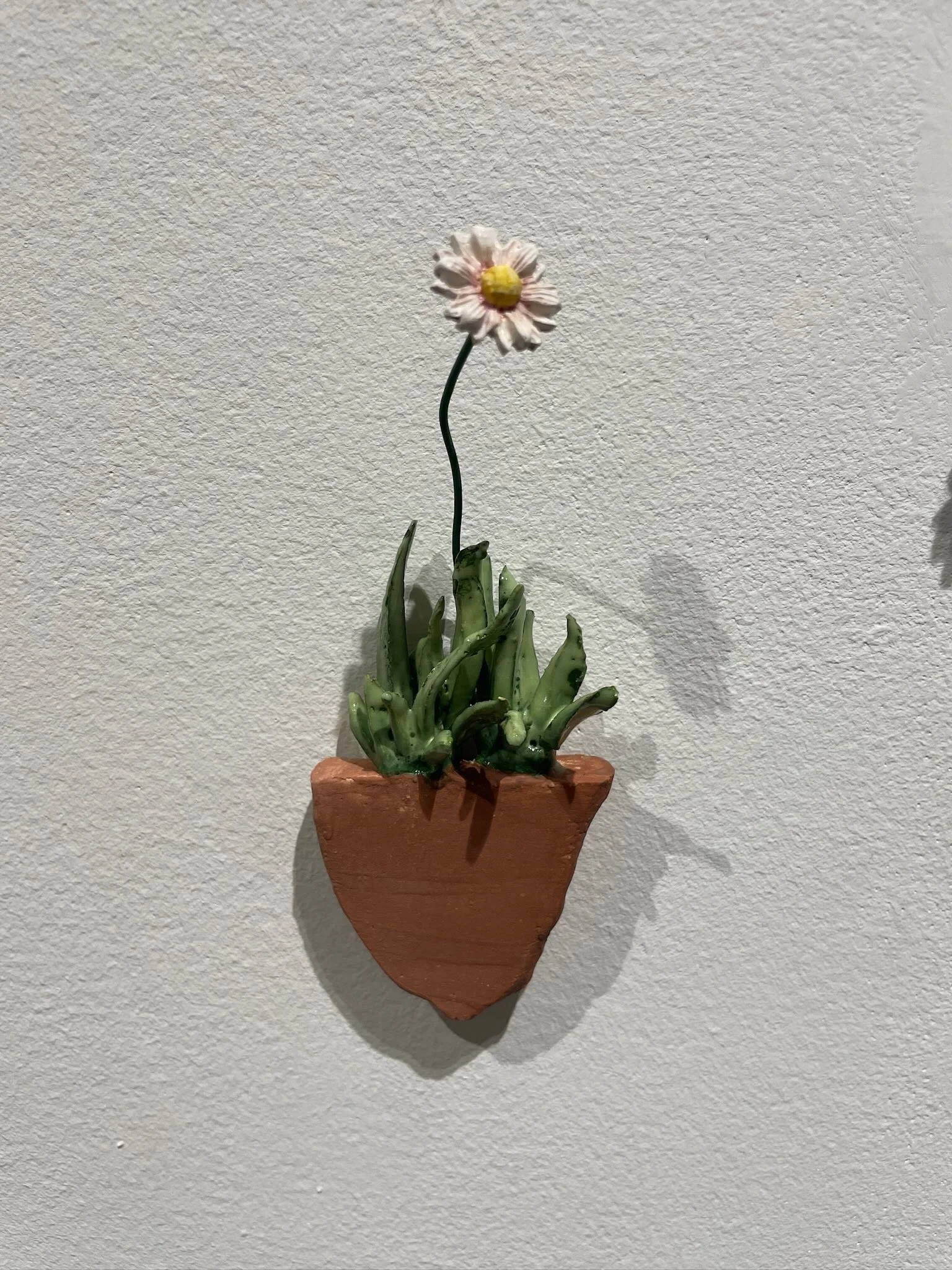 Wall-mounted ceramic pot with green succulent plant and a single artificial flower.