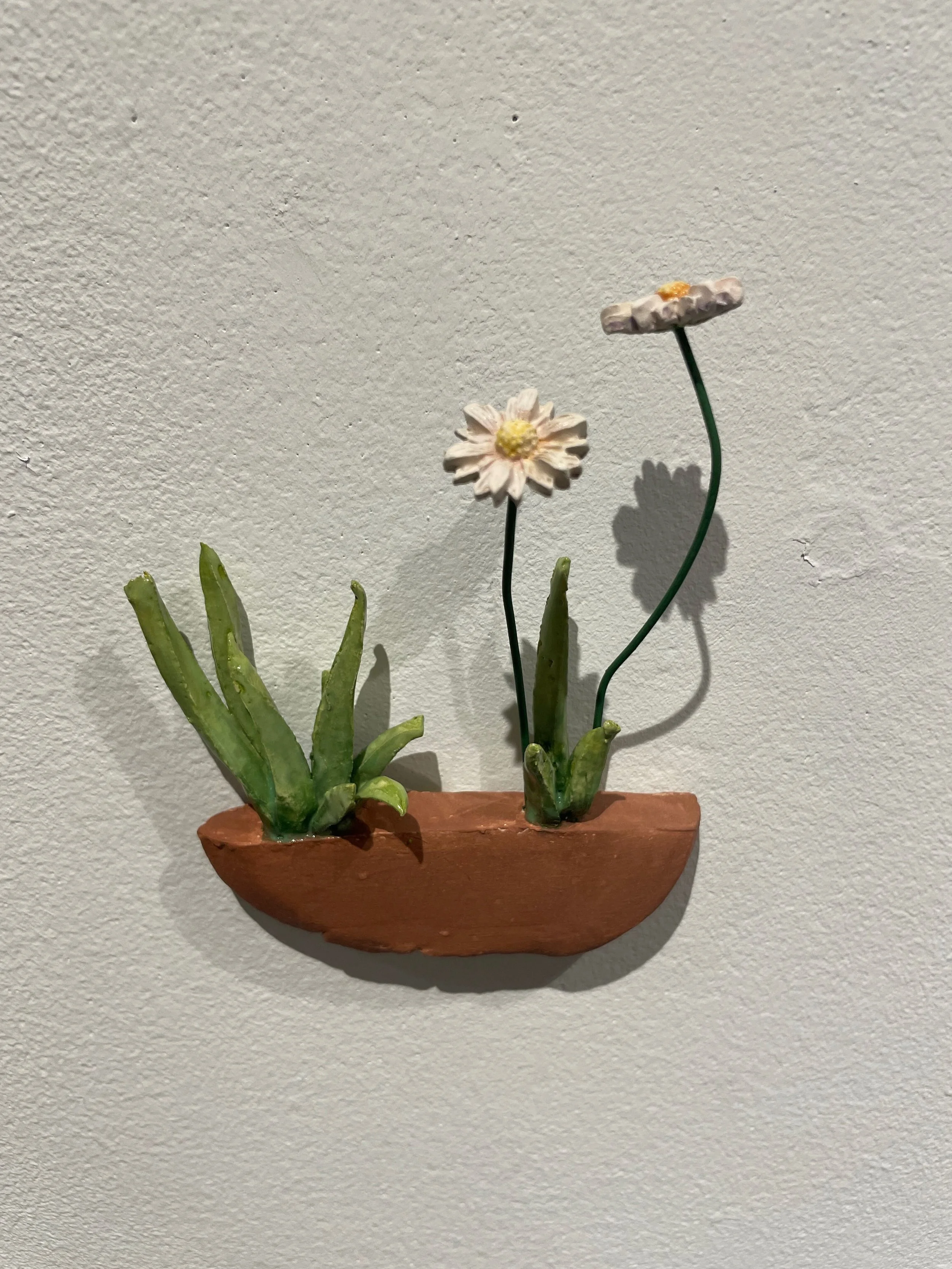 Decorative artificial plant with green leaves and white flowers on a terracotta wall-mounted container.