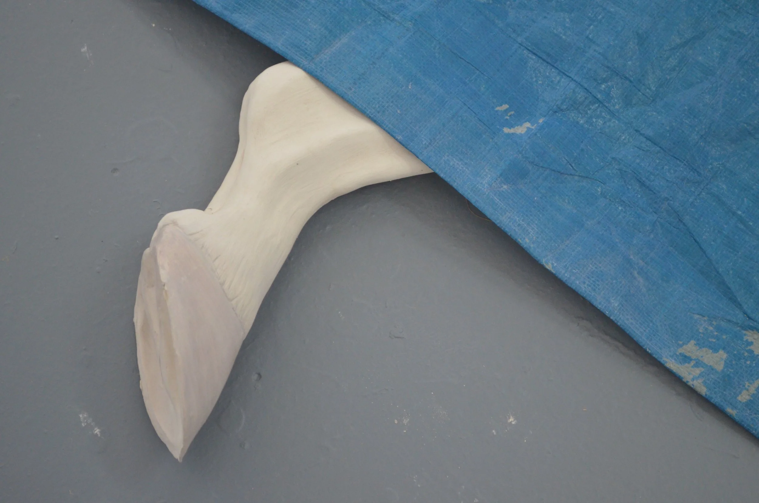 A white, curved whale sculpture partially concealed by a blue tarp on a gray floor.
